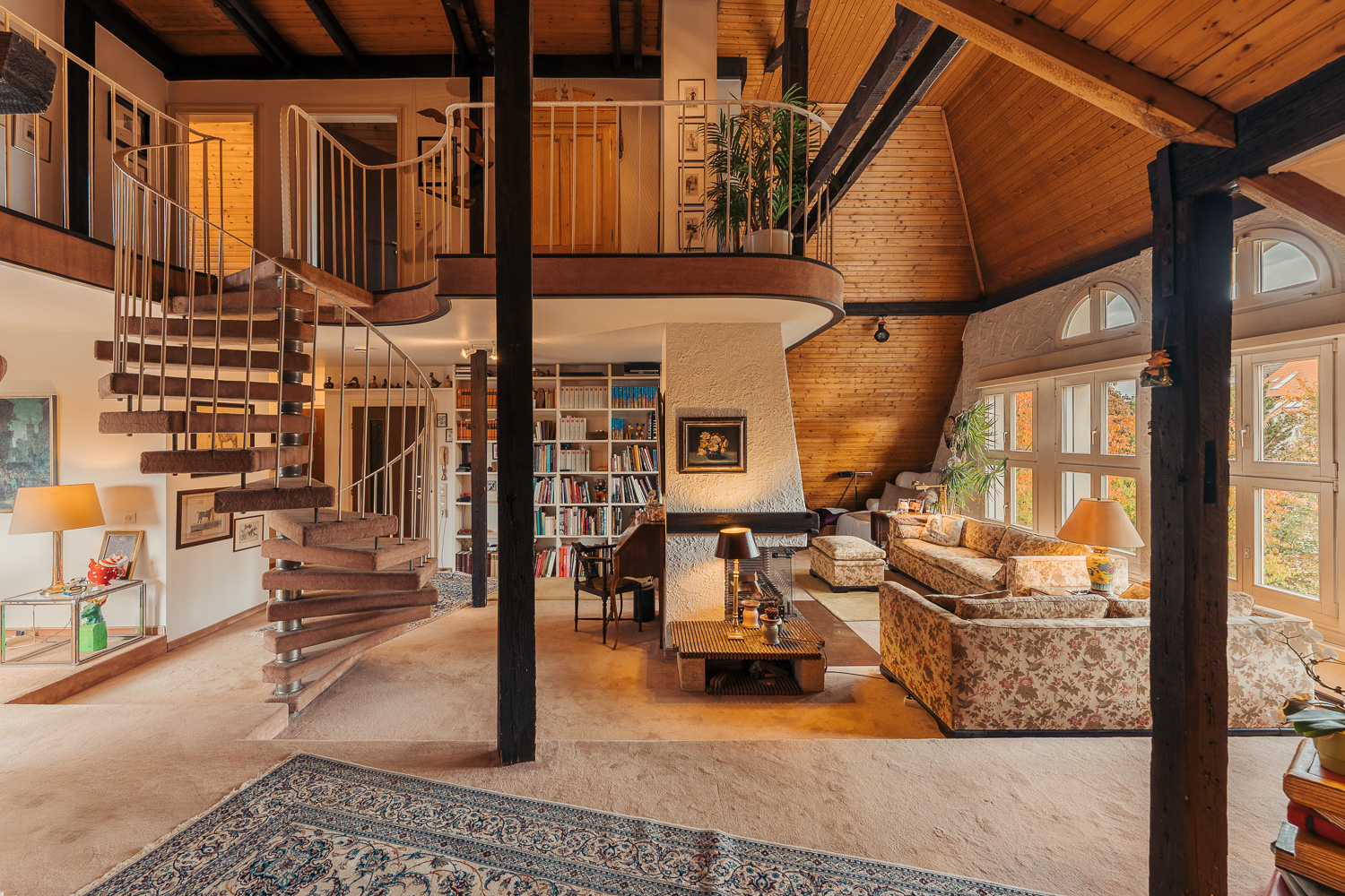 Helles Wohnzimmer mit Wendeltreppe, Bücherregal, Blumenmustermöbeln und großen Fenstern.