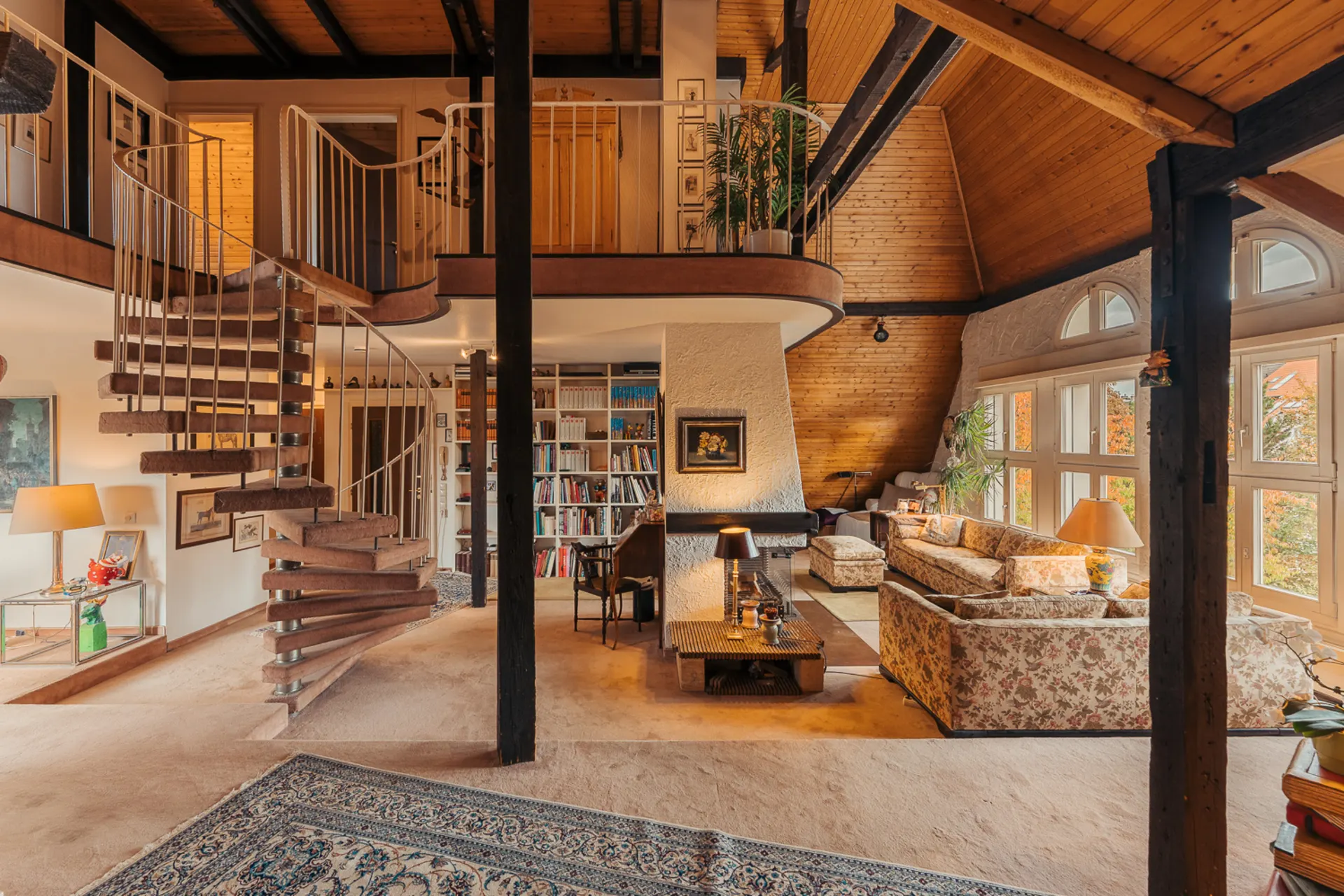 Helles Wohnzimmer mit Wendeltreppe, Bücherregal, Blumenmustermöbeln und großen Fenstern.