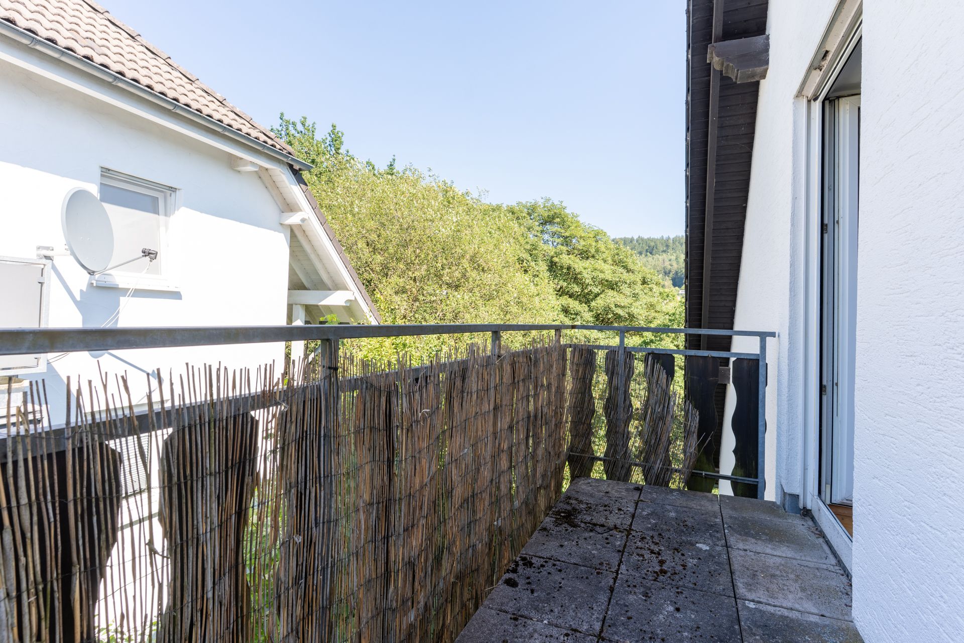 Kleiner Balkon mit Bambusverkleidung und Blick auf Bäume, daneben Nachbarhaus.