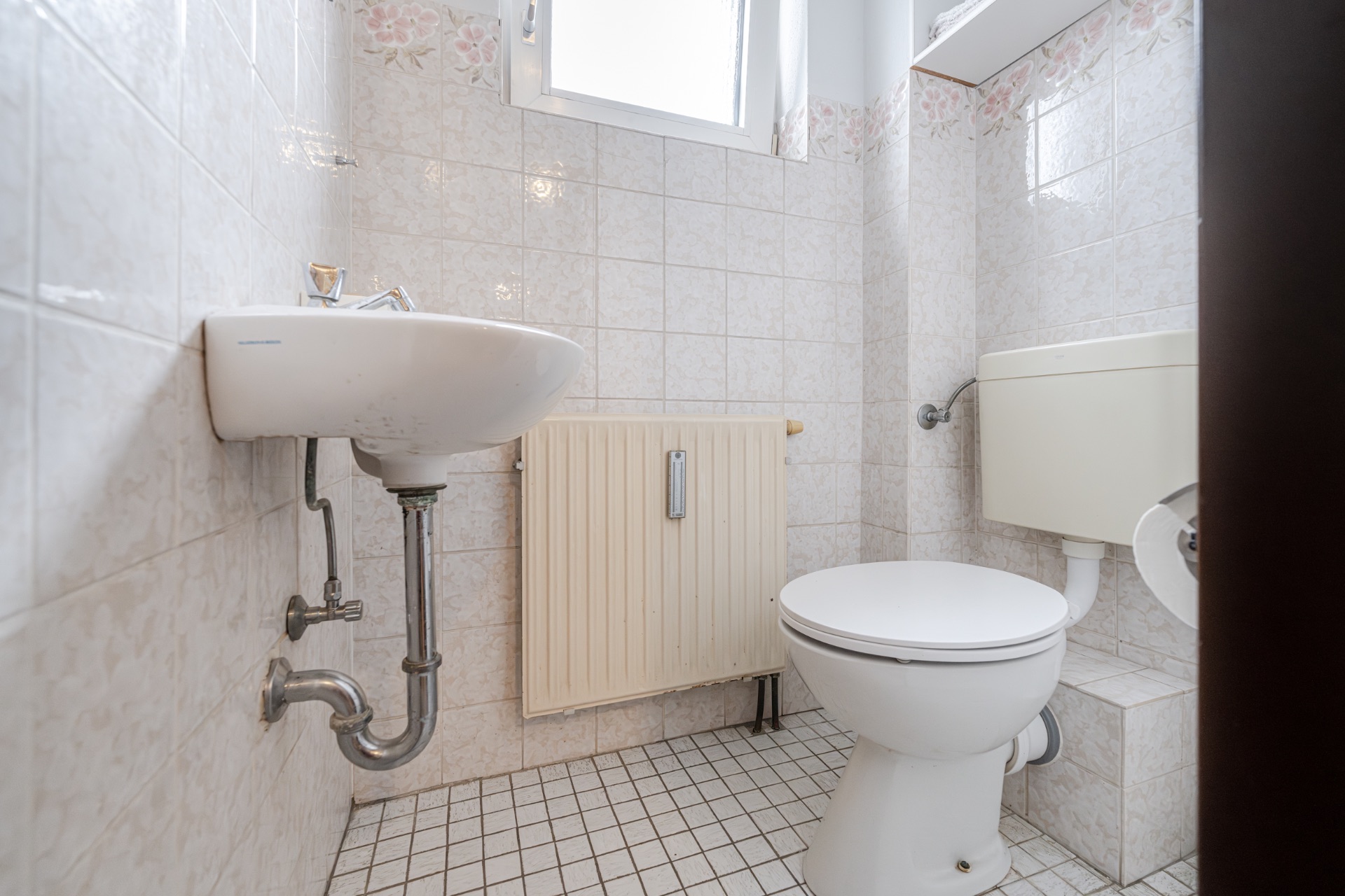 Kleines Badezimmer mit Toilette, Waschbecken, Heizkörper und gefliesten Wänden.