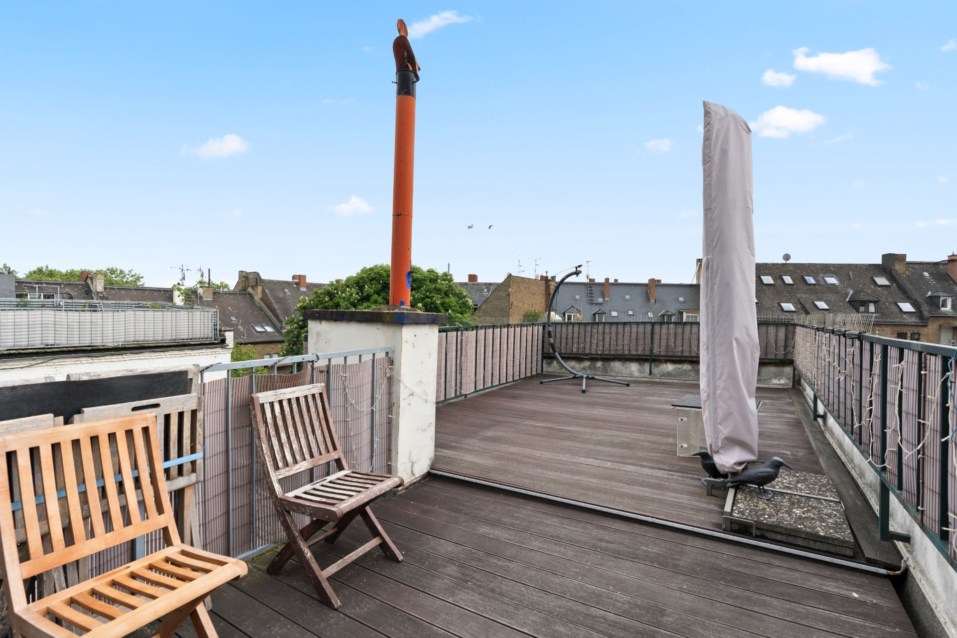 Dachterrasse mit Holzboden, zwei Stühlen und Ausblick auf umliegende Häuser.