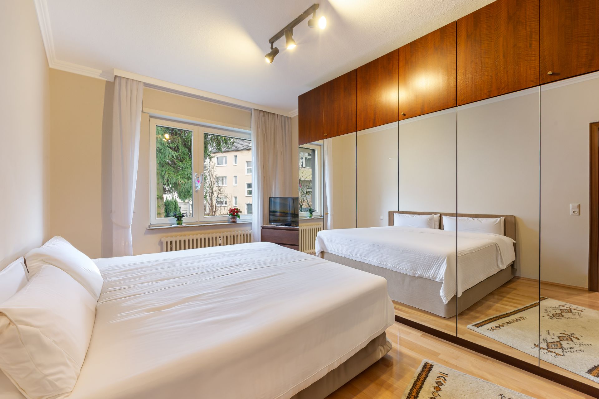Helles Schlafzimmer mit großem Bett, Spiegel-Schrank und Fenster mit Blick nach draußen.