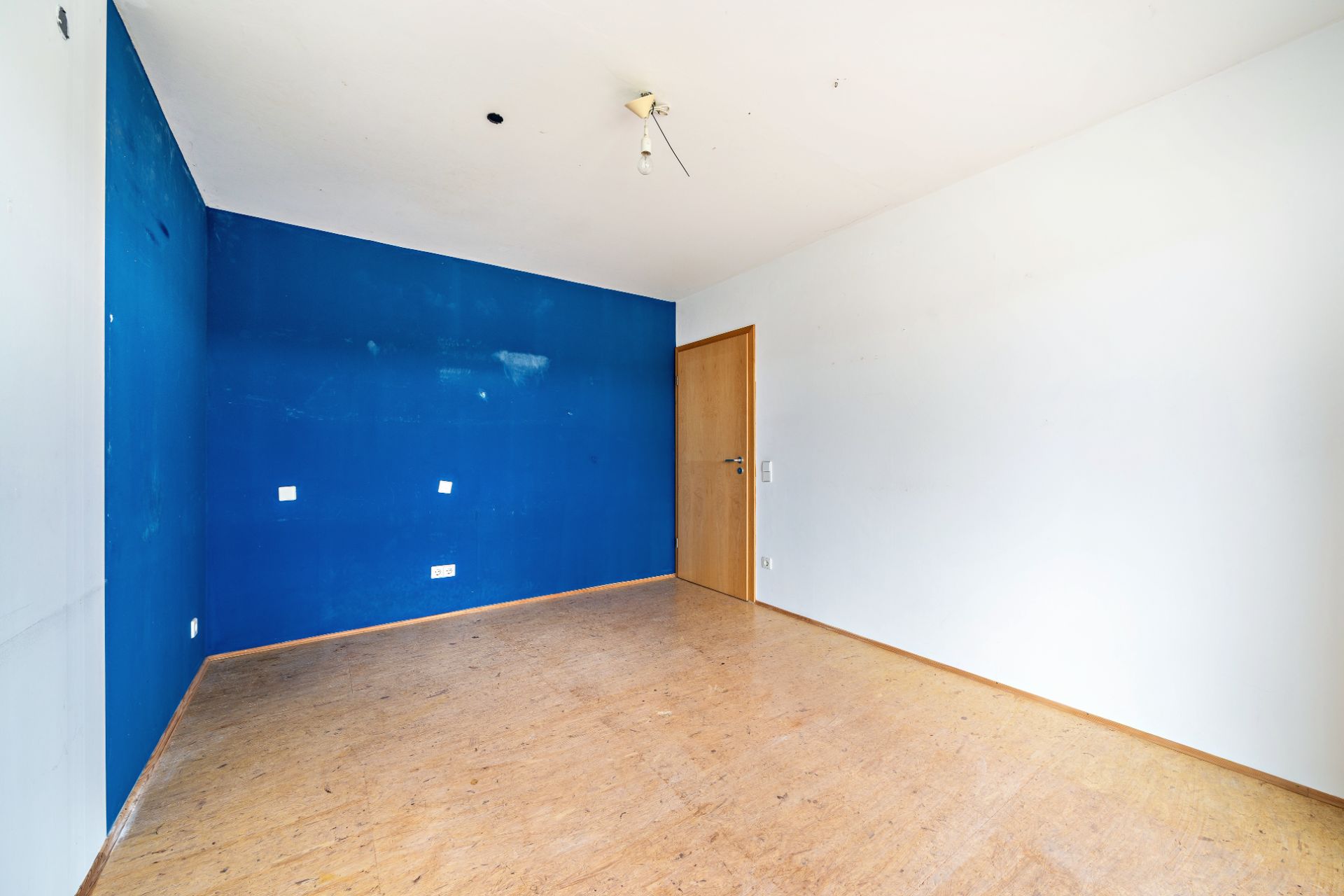 Leerer Raum mit Holzfußboden, einer blauen Wand und einer Holztür.