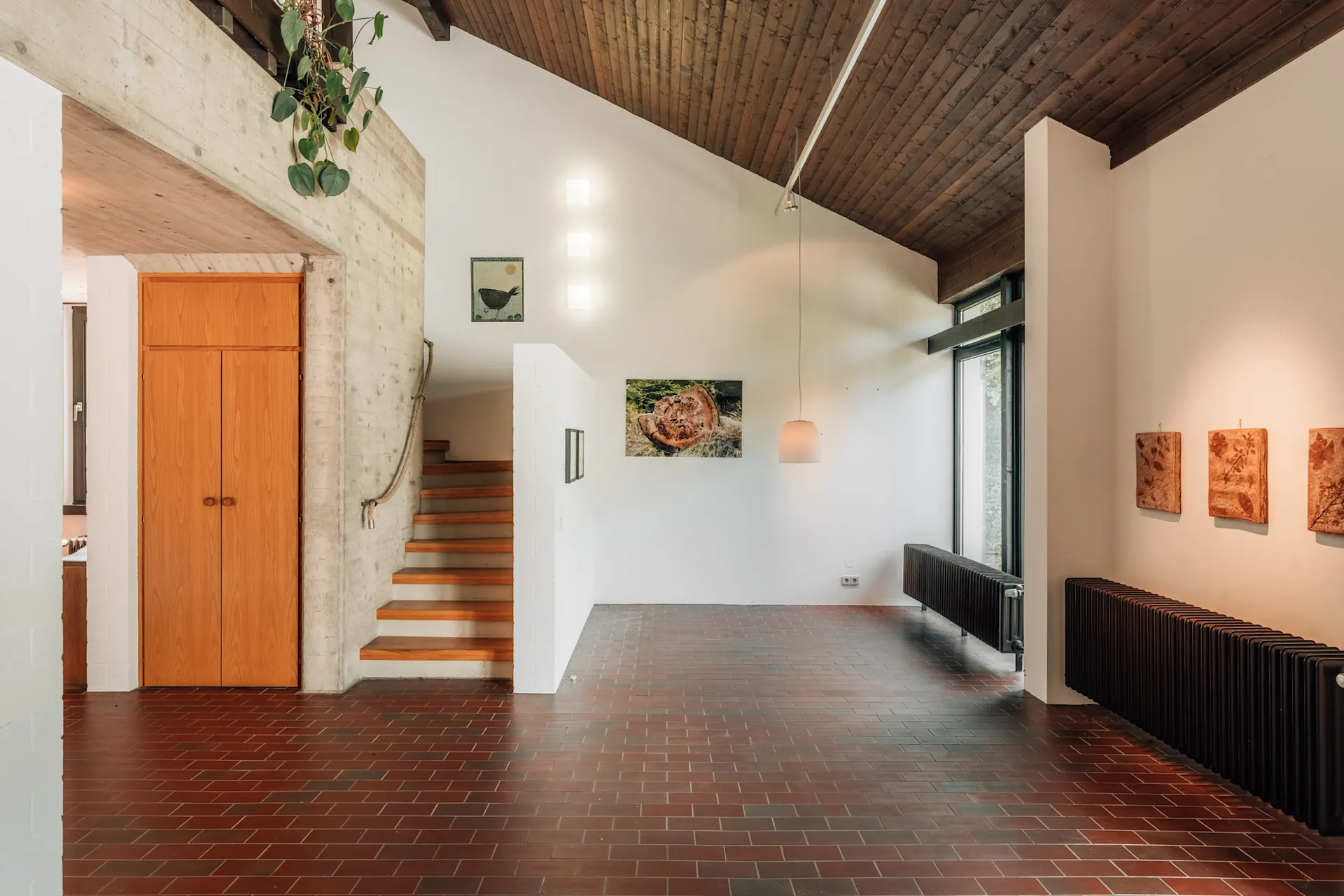 Innenraum mit Holztreppe, braunen Fliesen, weißen Wänden und Kunst an den Wänden.
