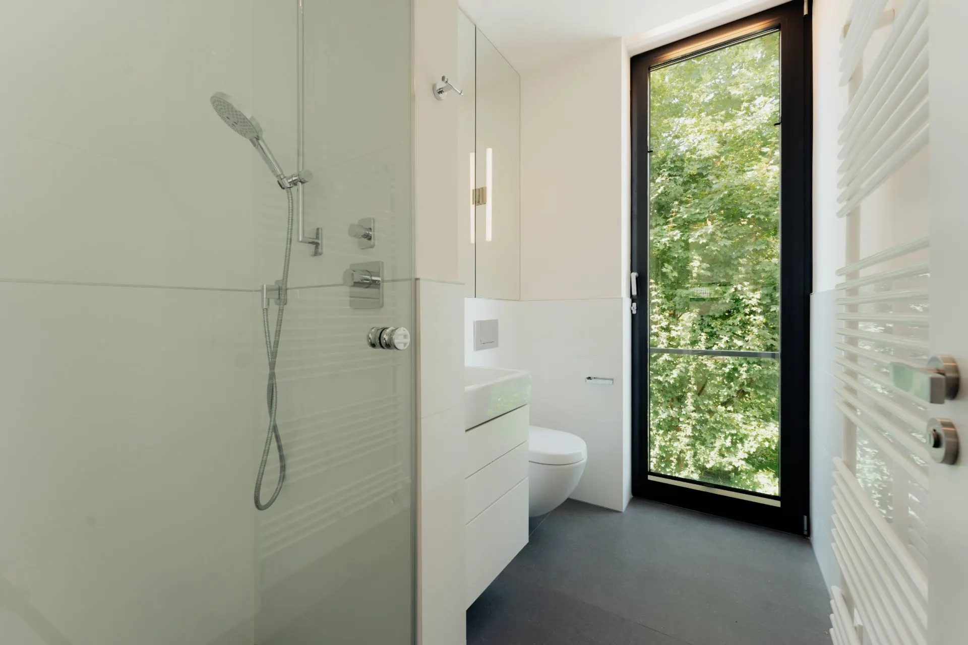 Modernes Bad mit Dusche, WC, Waschbecken und großem Fenster mit Blick ins Grüne.