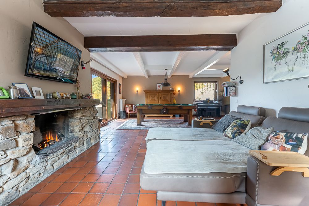 Wohnzimmer mit Kamin, Ecksofa, Billardtisch und Fliesenboden, große Fenster zur Terrasse.