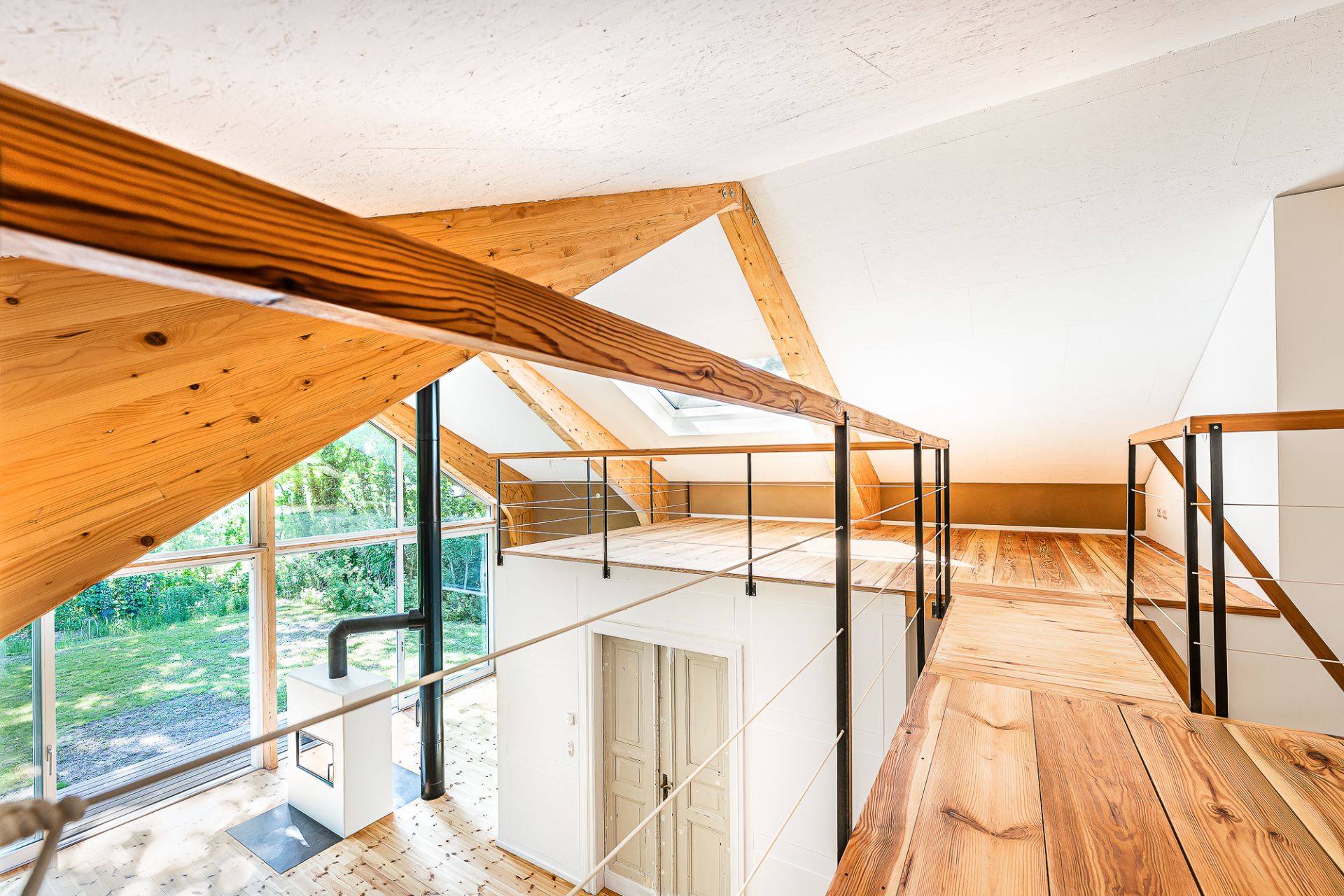 Modernes Dachgeschoss mit Holzgeländer, Sicht auf große Fenster und Holzfußboden.