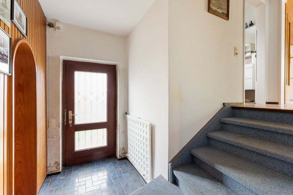 Eingangsbereich mit brauner Tür, blauen Fliesen und einer Treppe mit Teppichboden.