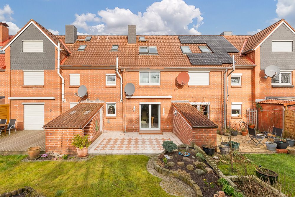 Rückseite eines roten Reihenhauses mit Terrasse, Garten und mehreren Satellitenschüsseln.
