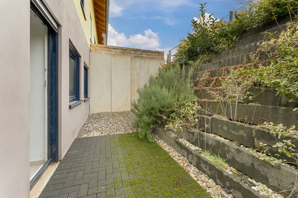 Kleiner gepflasterter Innenhof mit niedriger Mauer, Pflanzen und abgetrepptem Hang.