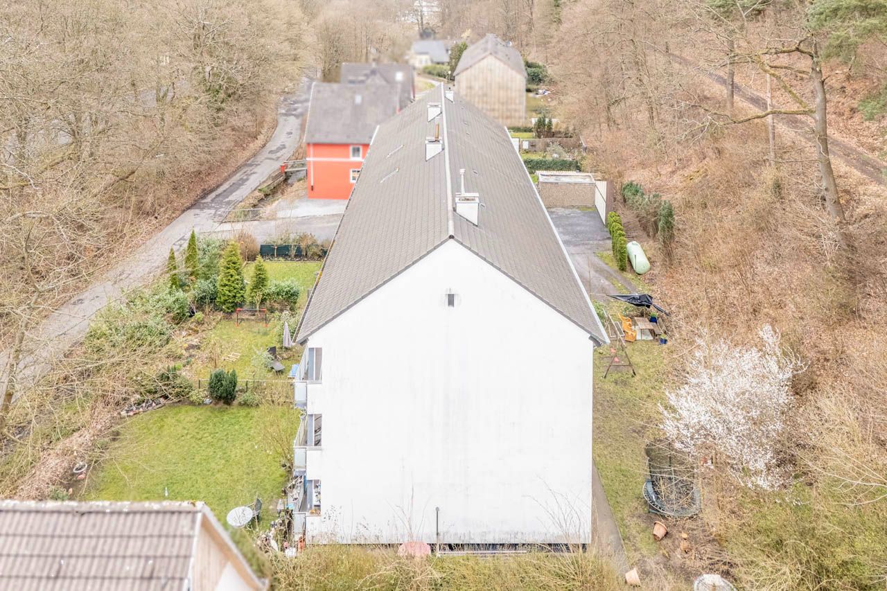 Blick von oben auf ein langes, weißes Wohnhaus mit Gärten an beiden Seiten.