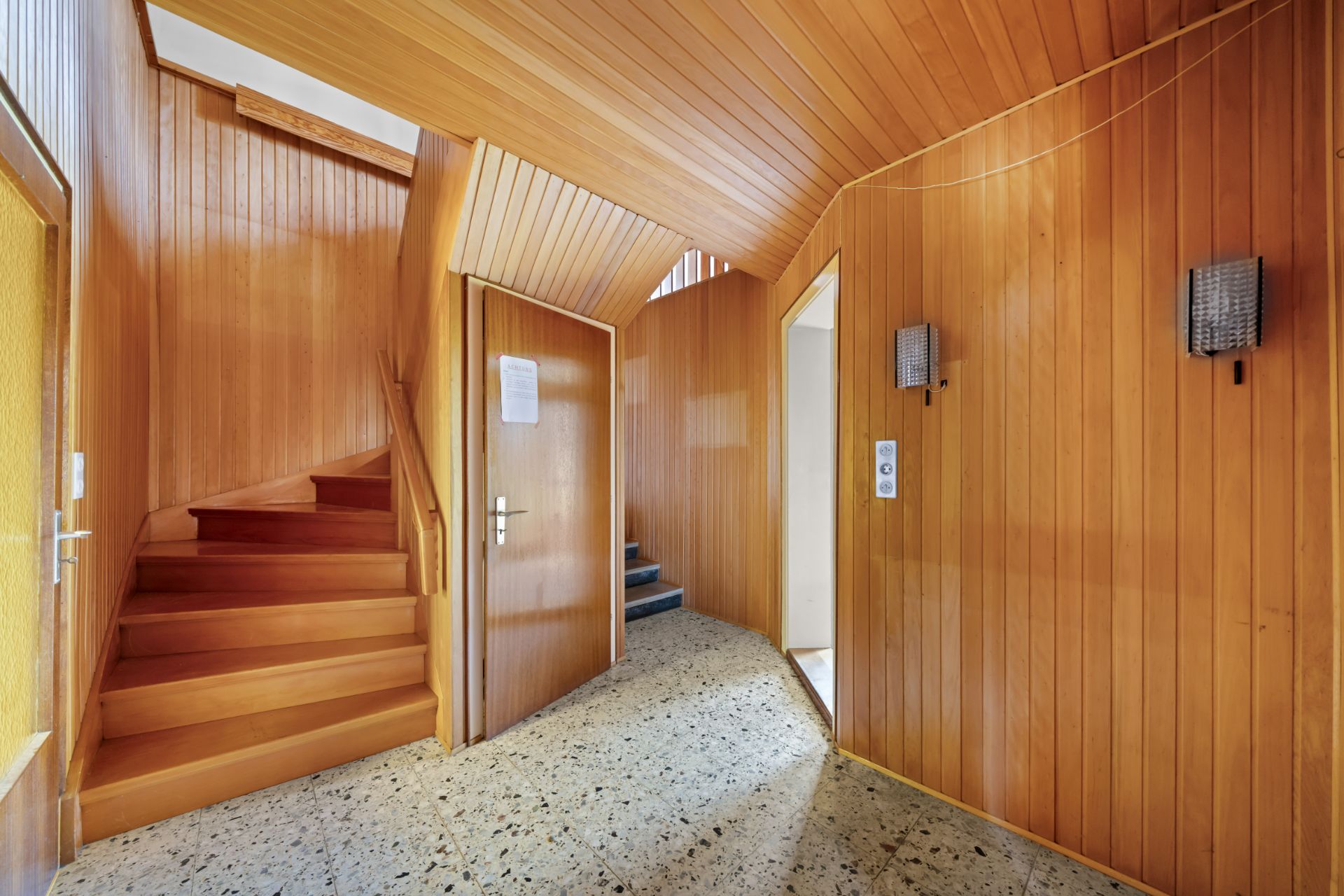 Flur mit Holzvertäfelung, mehreren Türen und einer Treppe nach oben.