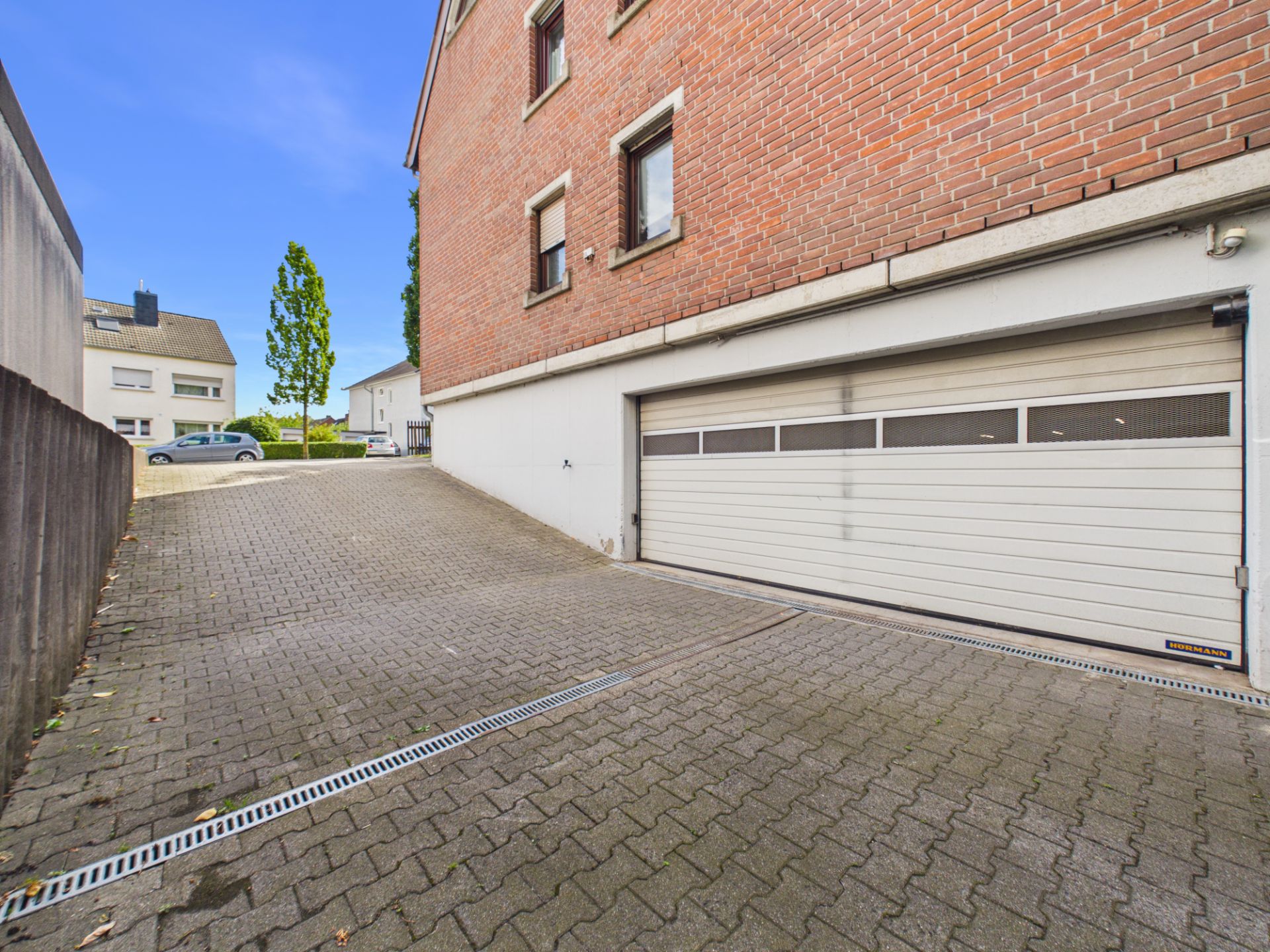 Einfahrt mit Pflastersteinen zu einer großen weißen Garage an einem Wohngebäude.