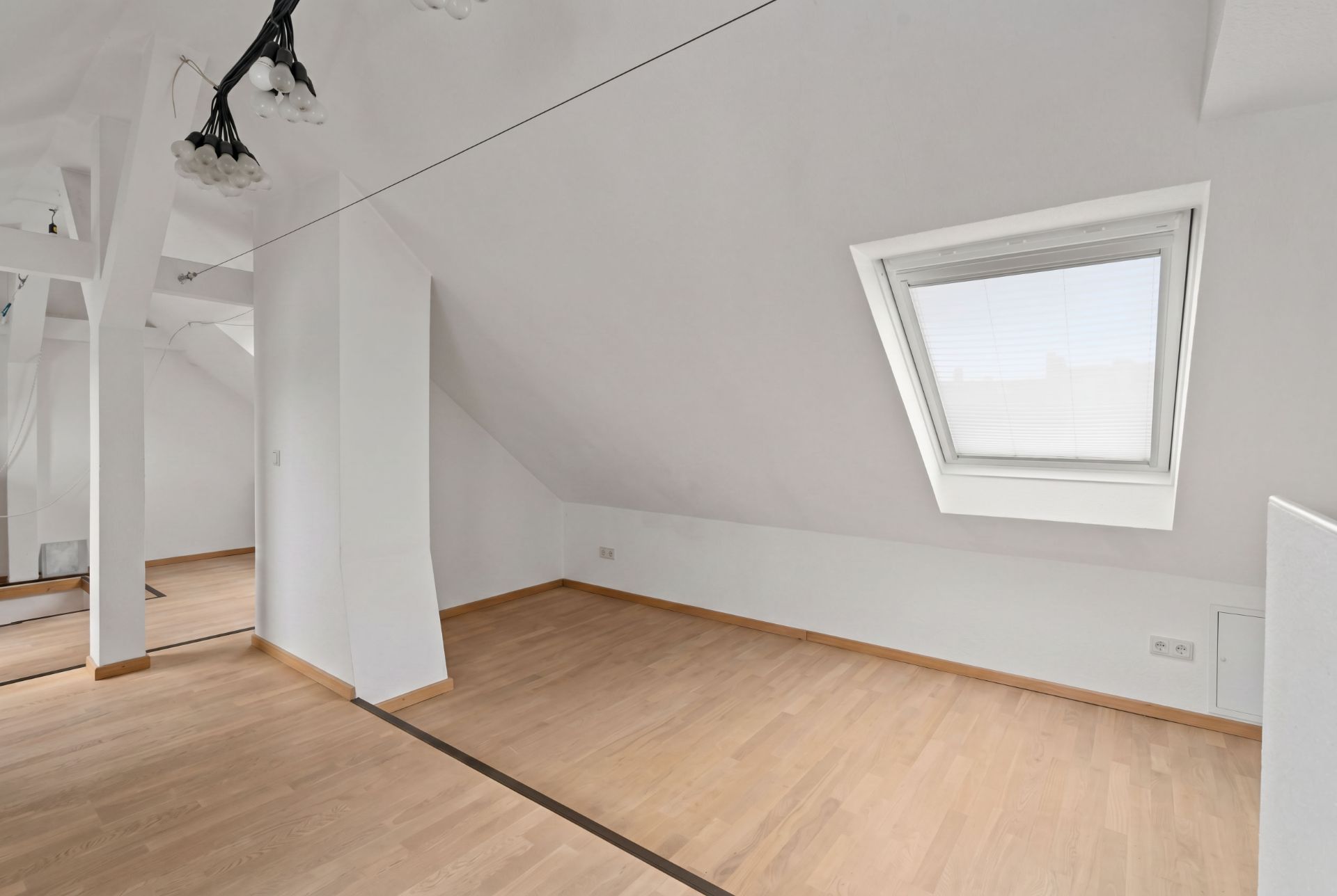 Heller Dachbodenraum mit Holzfußboden, schräger Wand und Dachfenster.