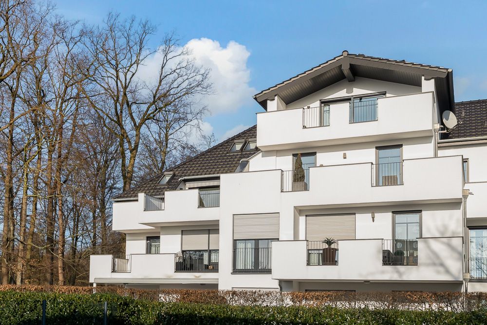 Modernes Wohnhaus mit Balkonen und großen Fenstern, im Vordergrund Bäume und Büsche.