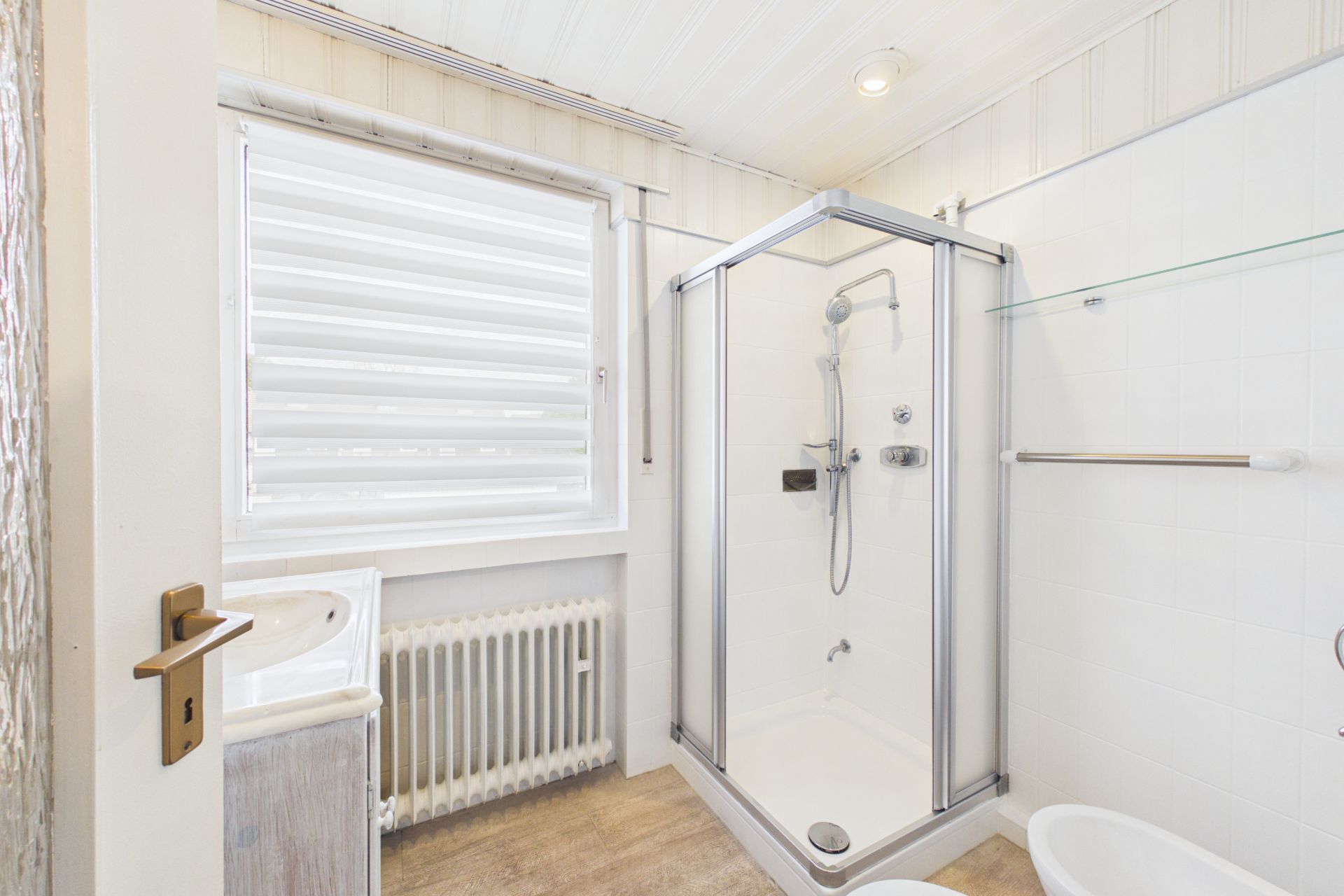 Helles Badezimmer mit Dusche, Waschbecken, Fenster und Handtuchhalter.