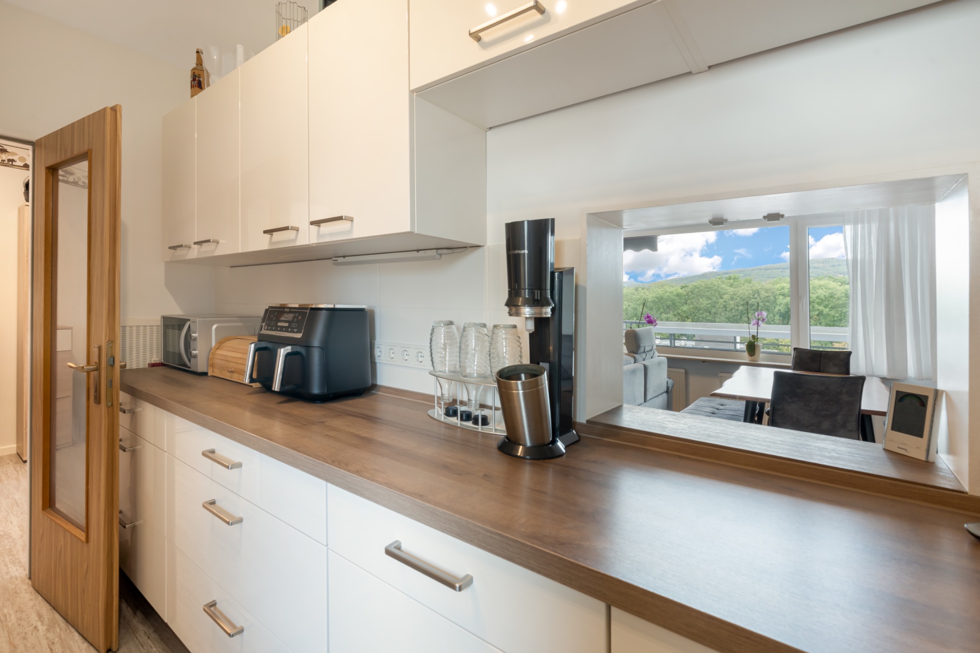 Moderne Küche mit weißen Schränken, Holztresen, Kaffeemaschine, Toaster und Blick ins Esszimmer.