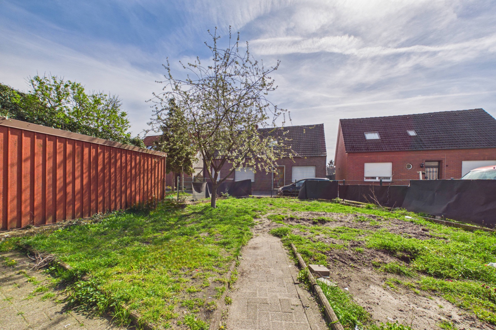 Garten mit Rasen, Baum, Gehweg und angrenzenden Häusern im Hintergrund.