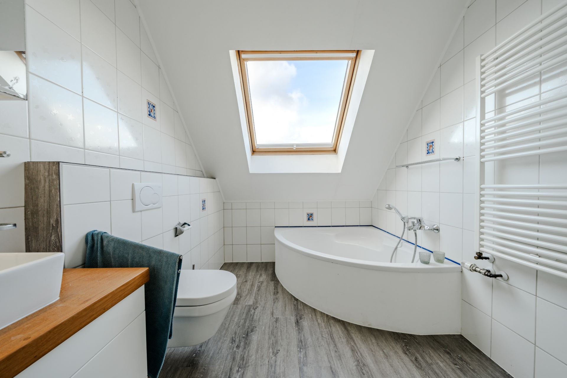 Helles Badezimmer mit Dachfenster, Badewanne, WC und Waschtisch auf Holzfußboden.