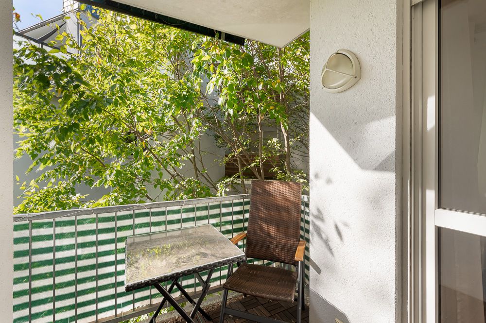 Kleiner Balkon mit Tisch, Stuhl und grüner Bepflanzung im Hintergrund.
