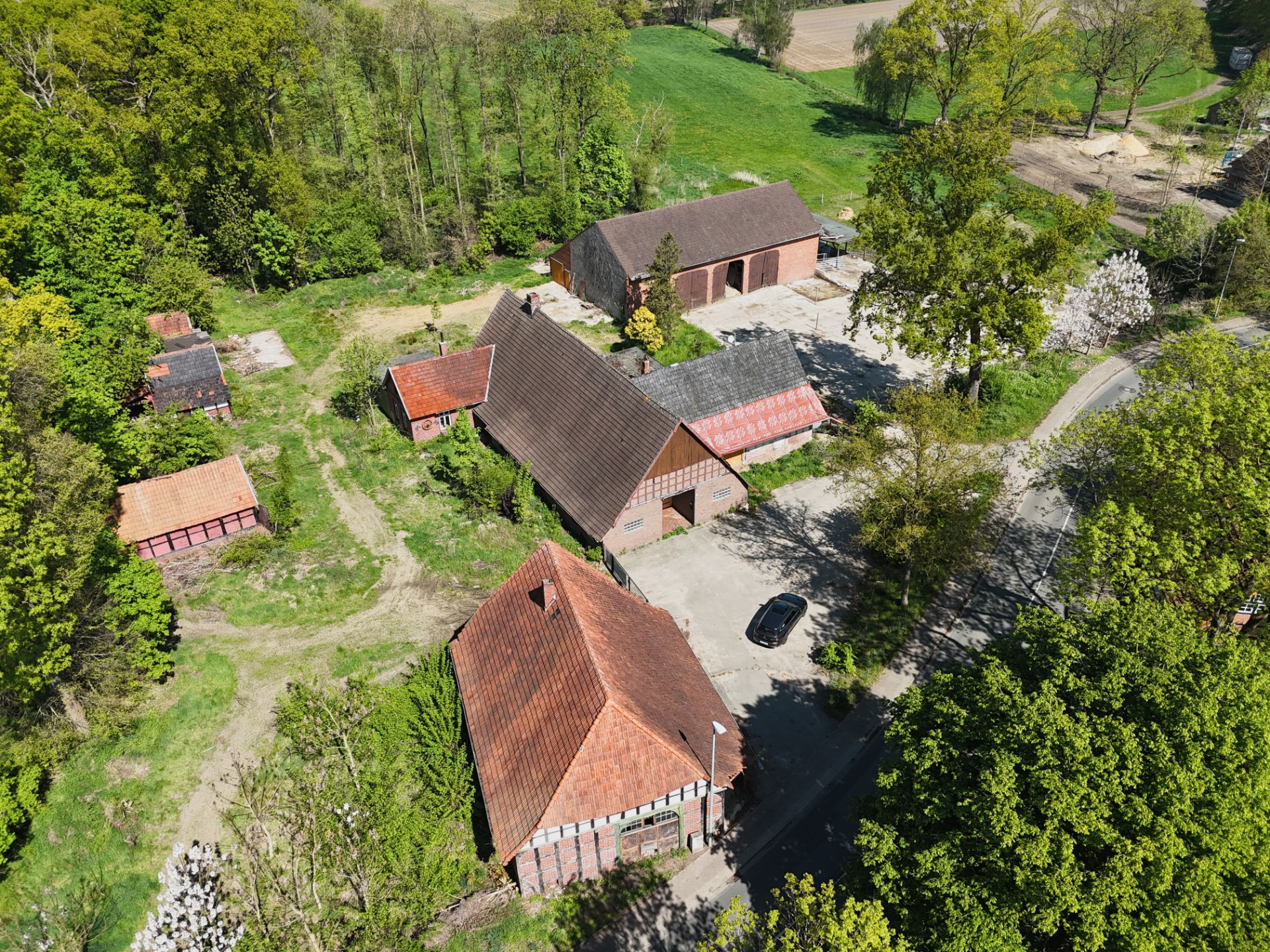 Luftaufnahme mehrerer Backsteingebäude mit roten Dächern in ländlicher Umgebung und viel Grün.