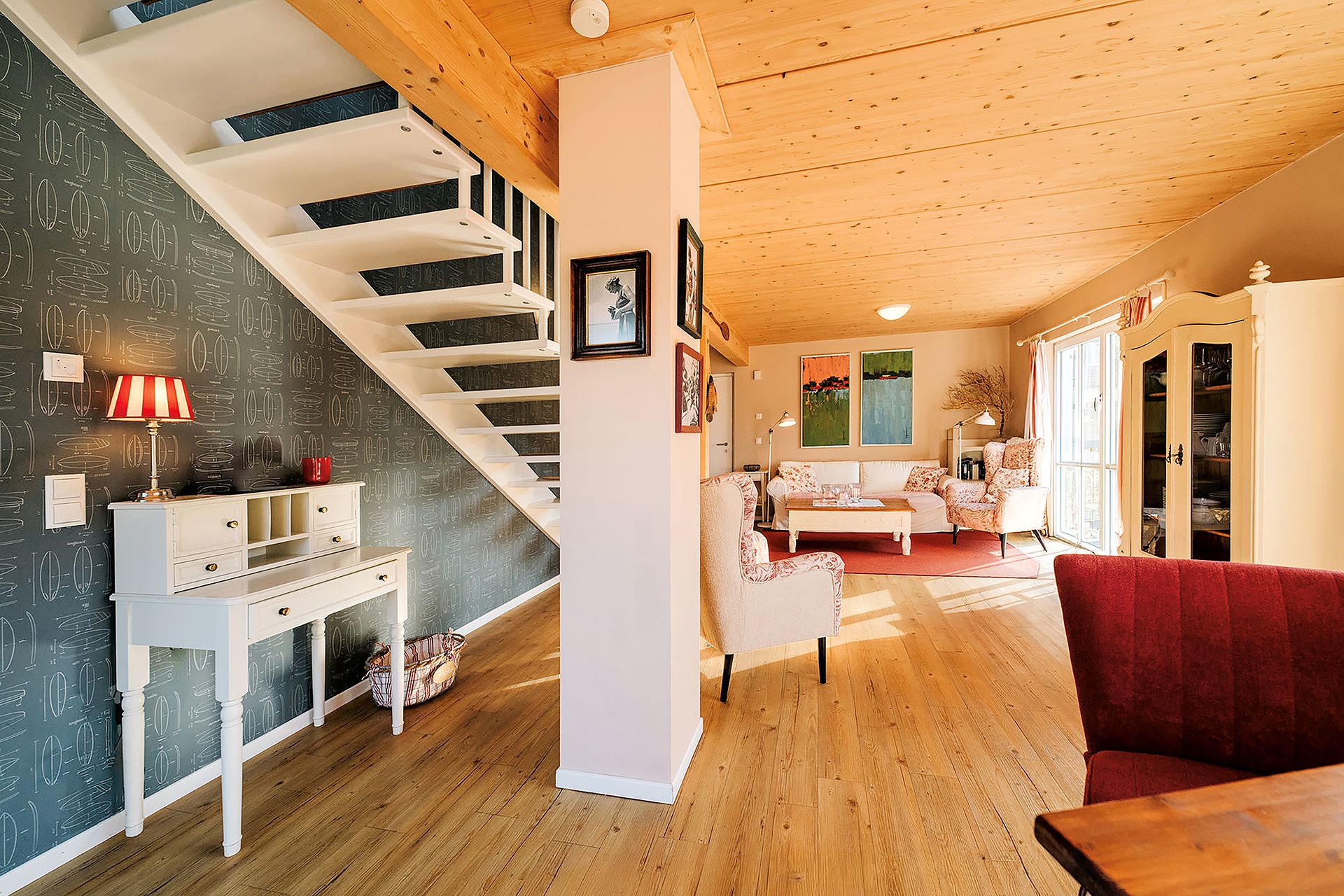 Helles Wohnzimmer mit Holzdecke, Treppe, Schreibtisch und Sitzbereich mit Sofa und Sesseln.