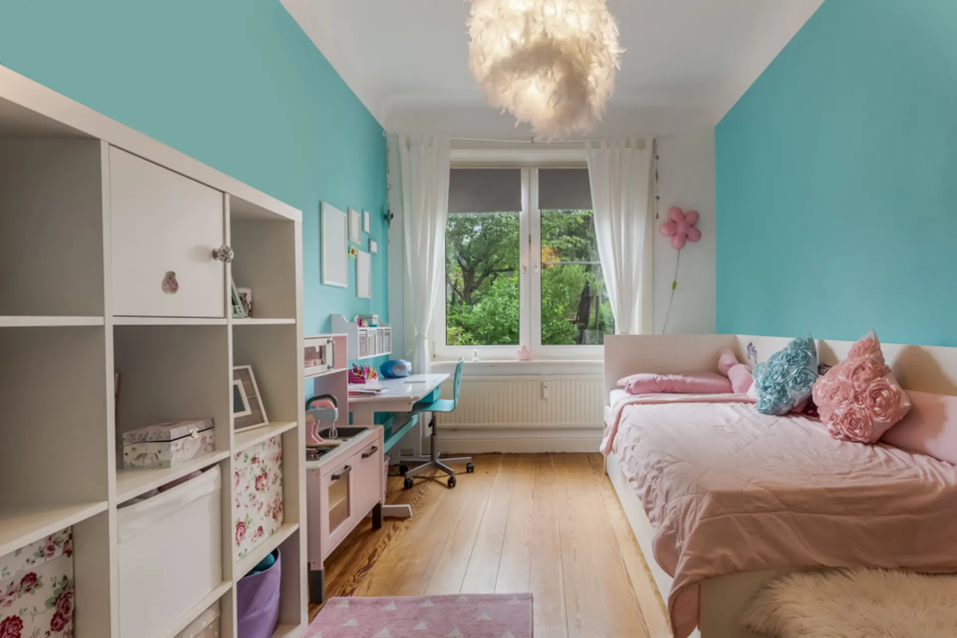 Helles Kinderzimmer mit türkisen Wänden, Einzelbett, Schreibtisch und Regal, großes Fenster mit Blick ins Grüne.