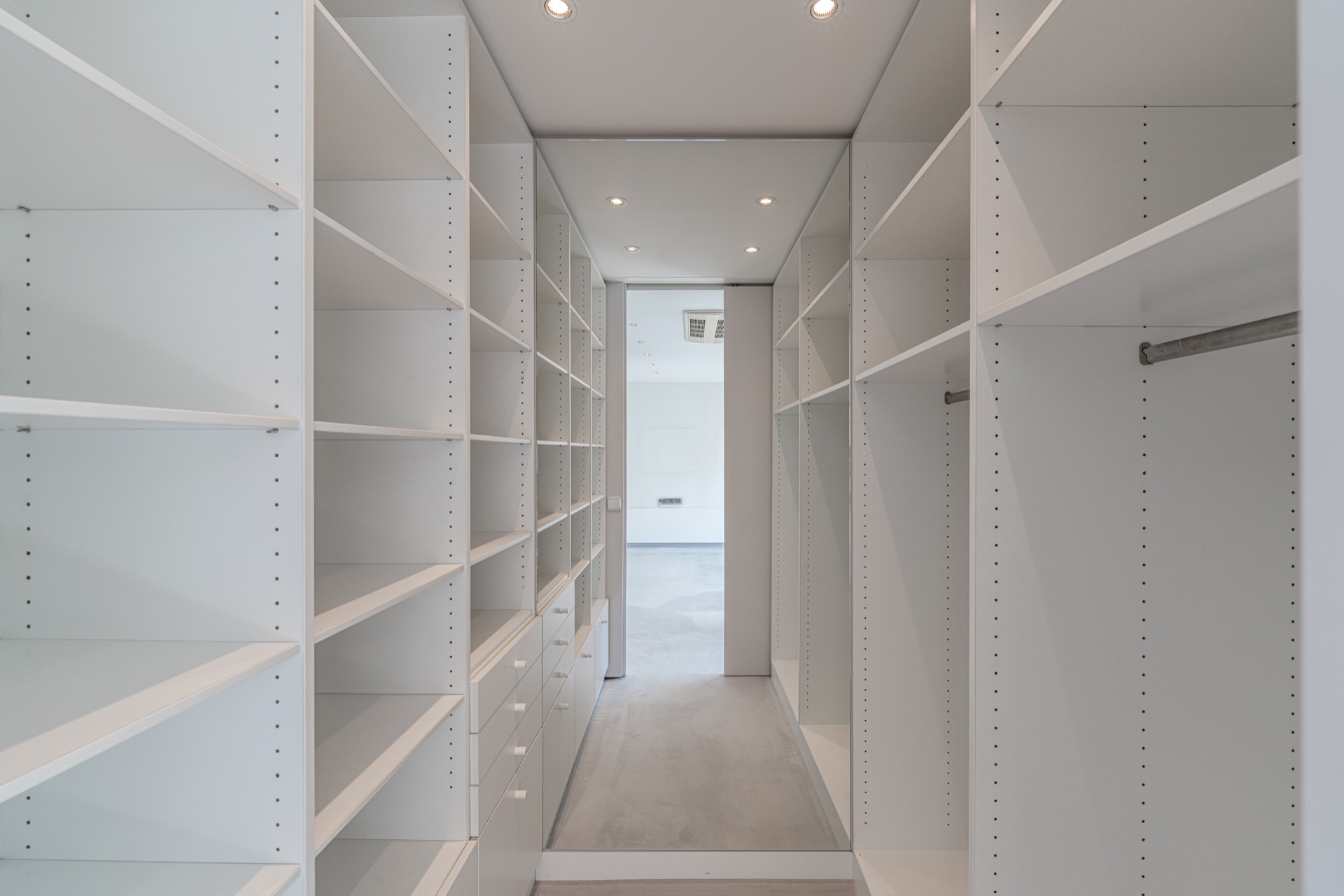 Begehbarer Kleiderschrank mit weißen Regalen und Schubladen, leer und gut beleuchtet.