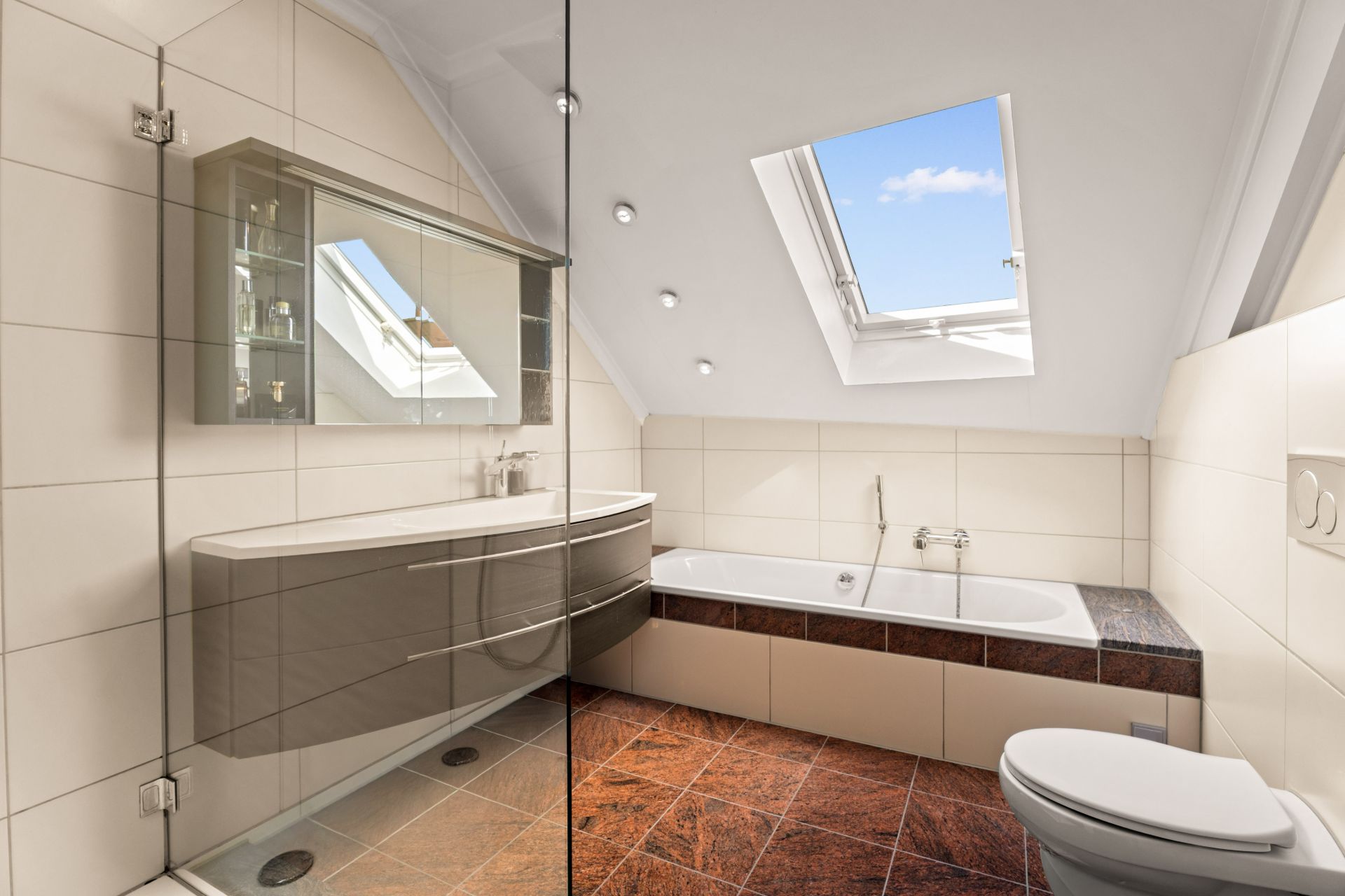 Modernes Badezimmer mit Badewanne, Dusche, Waschbecken, WC und Dachfenster.