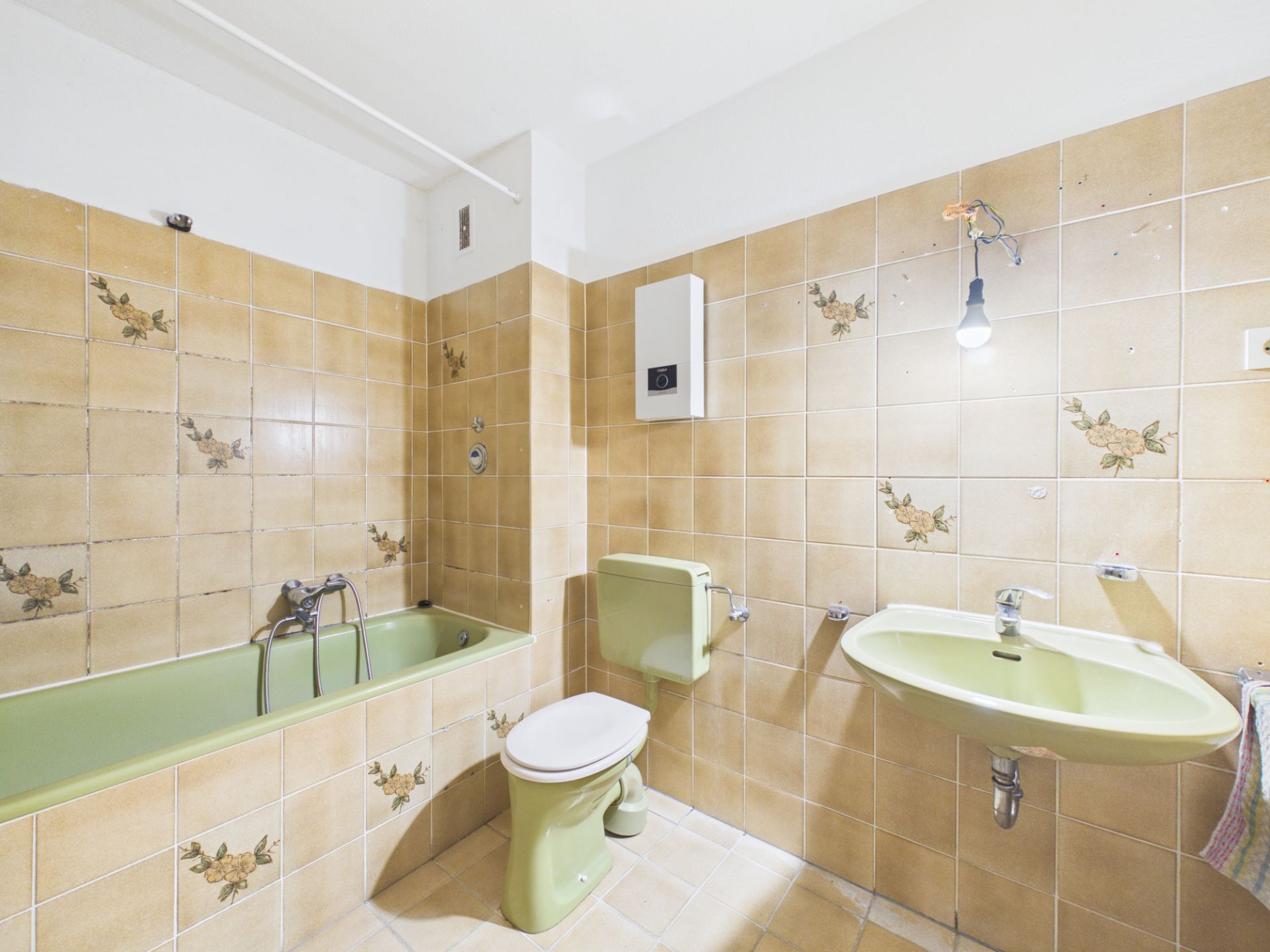Bad mit grüner Badewanne, Toilette und Waschbecken, gefliest mit beigen Fliesen mit Blumenmuster.