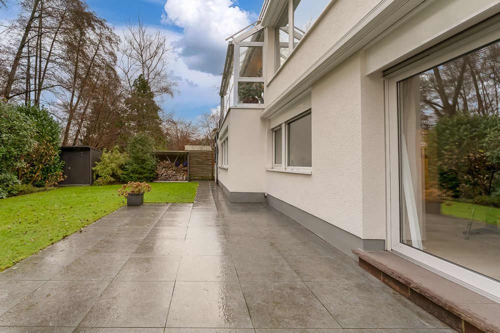 Nasse Terrasse neben einem modernen Wohnhaus mit Garten, Rasen und kleinem Schuppen.
