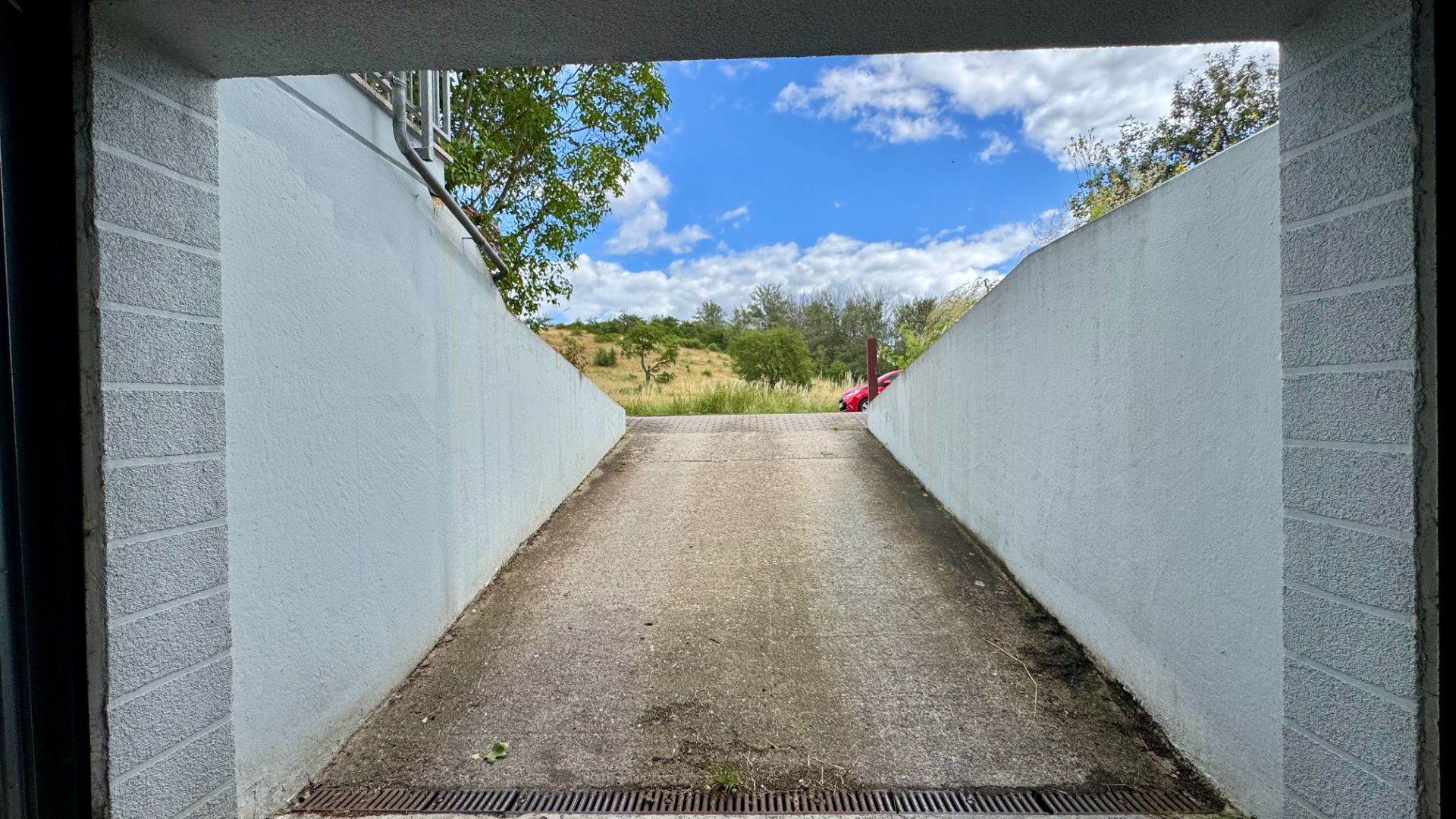 Blick aus einer Garage auf eine Auffahrt mit weißen Wänden und blauem Himmel im Hintergrund.