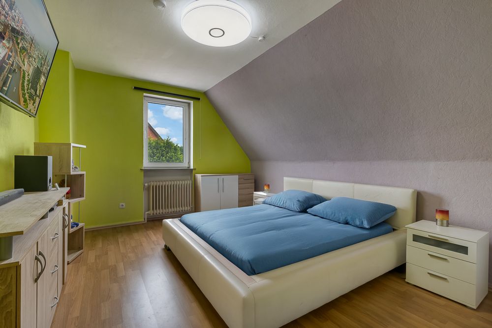 Helles Schlafzimmer mit großem Bett, Nachttischen, Kommode, Fenster und Fernseher an der Wand.
