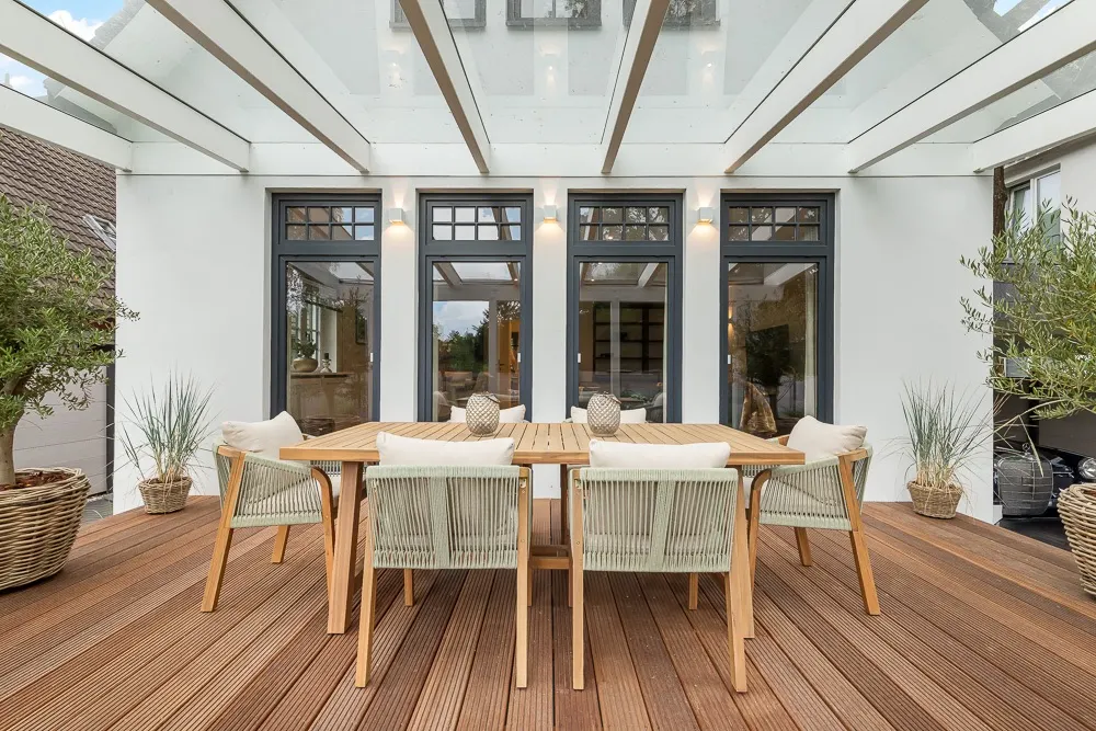 Überdachte Holzterrasse mit Esstisch, sechs Stühlen und Pflanzen in Körben.