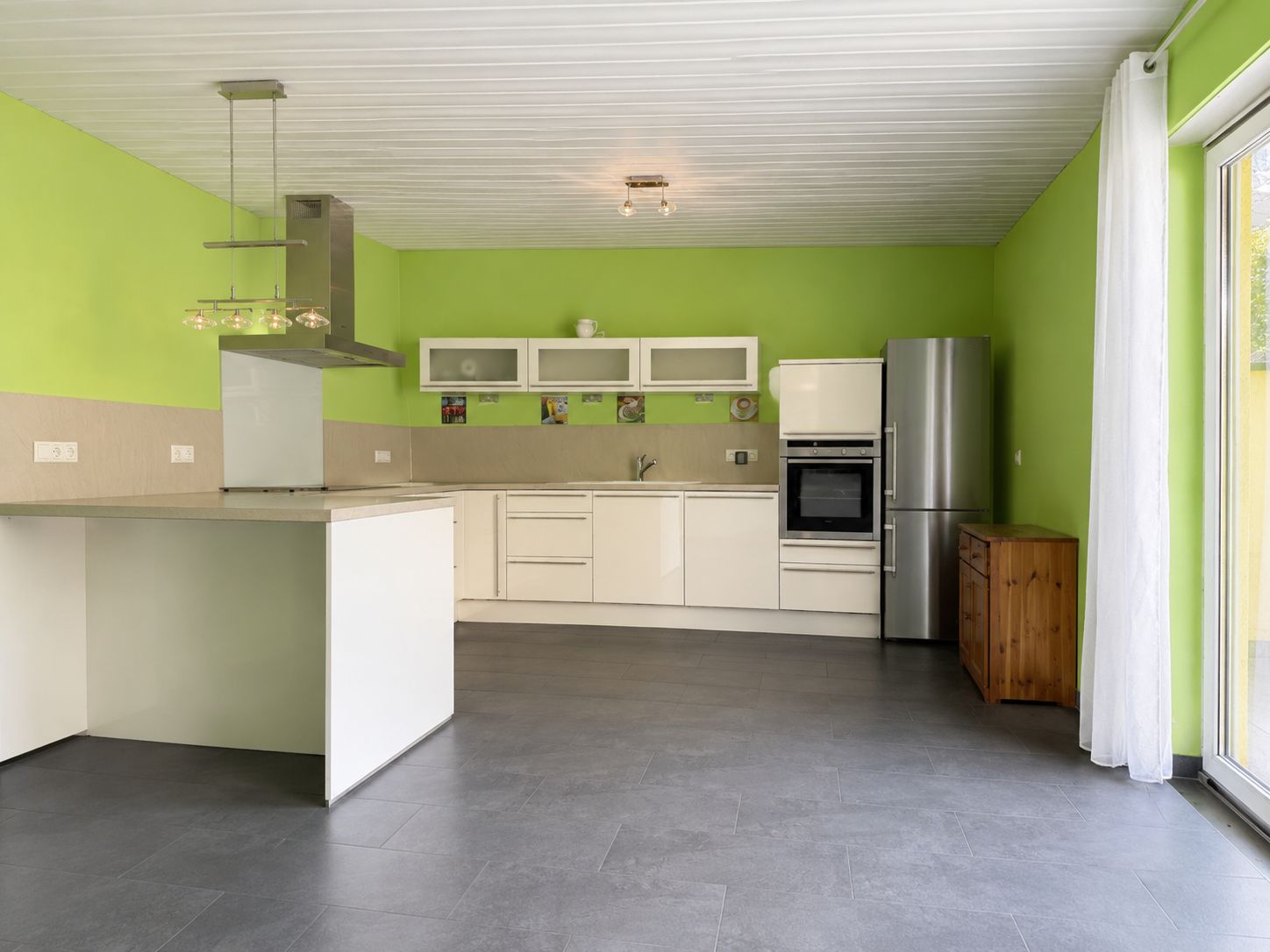 Moderne Küche mit grünen Wänden, weißer Einrichtung, Kücheninsel und großem Fenster.