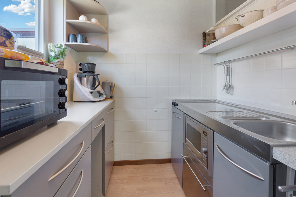 Moderne, schmale Küche mit Küchengeräten, grauen Schränken und einem Fenster.