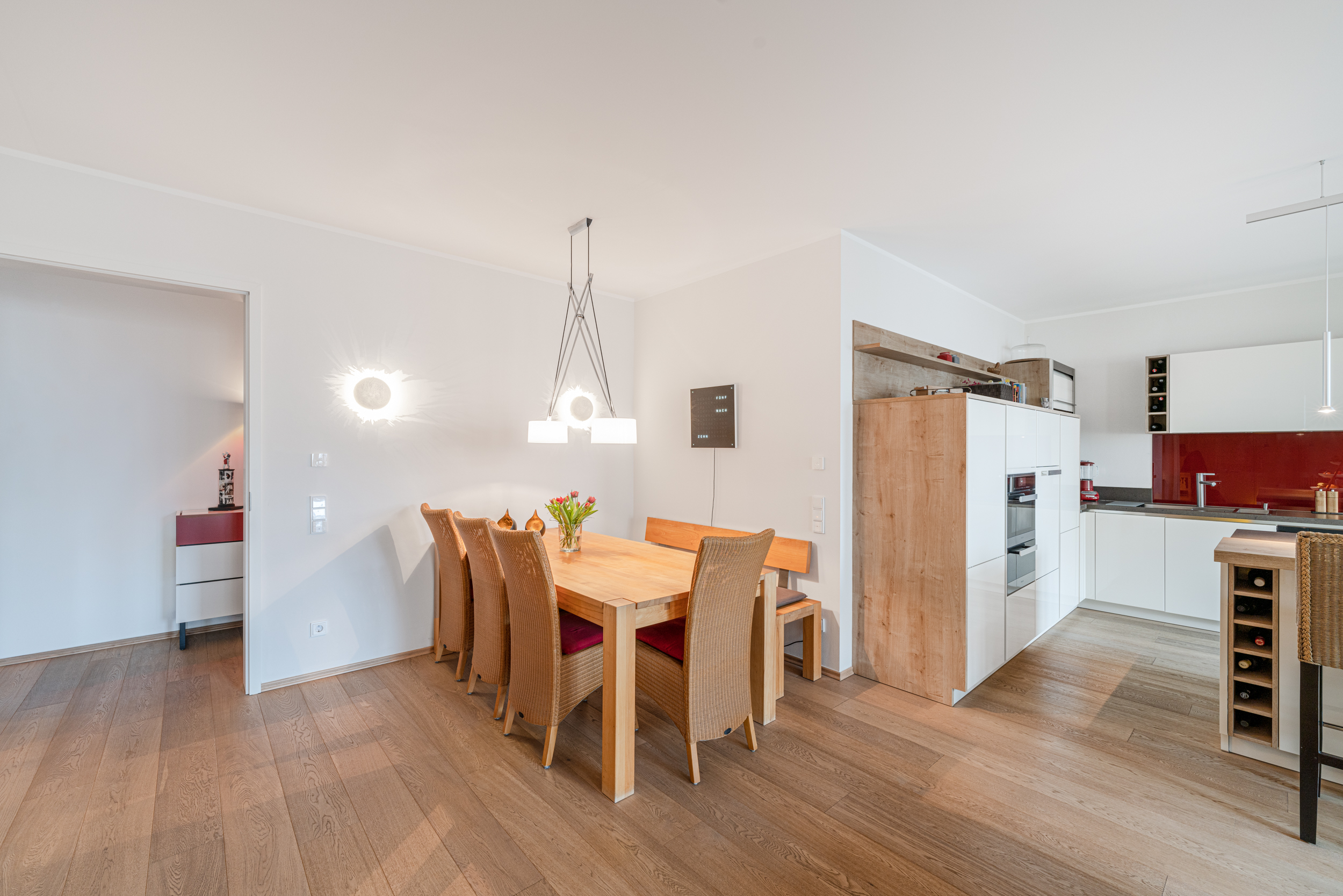 Essbereich mit Holztisch, sechs Stühlen, Bank und moderner Einbauküche im Hintergrund.