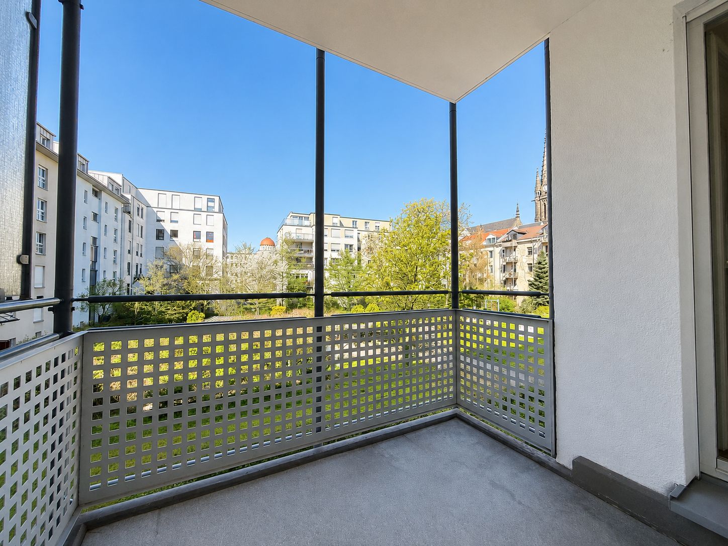 Blick von einem überdachten Balkon auf grüne Bäume und umliegende Wohngebäude.