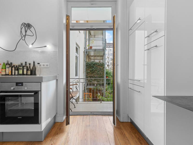 Moderne Küche mit Holzboden und offenem Zugang zu einem kleinen Balkon mit Blick ins Grüne.