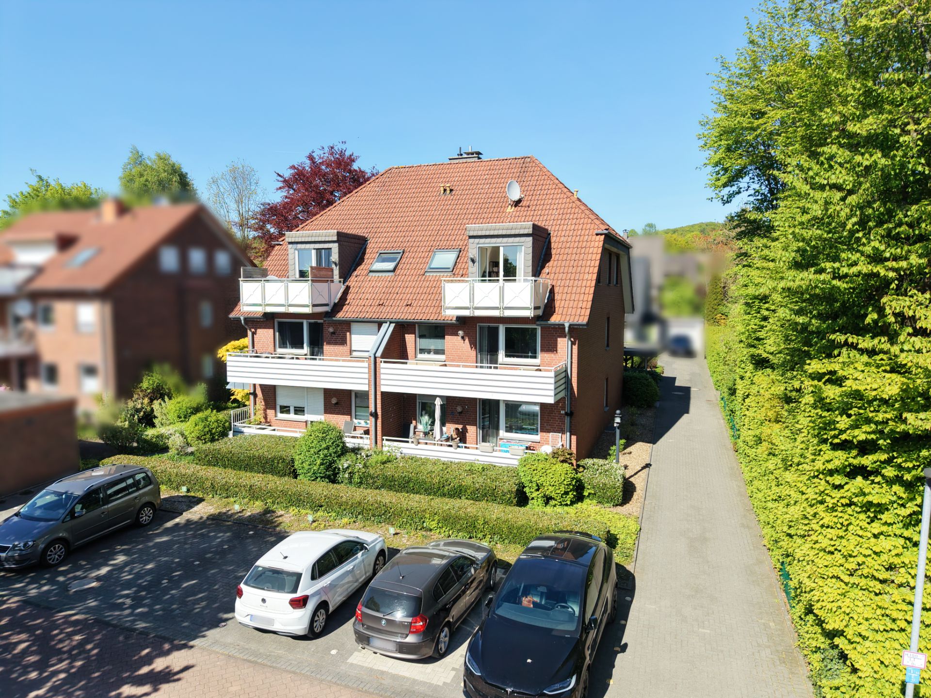 Mehrfamilienhaus mit Balkonen und Vorgarten, mehrere Autos parken davor.