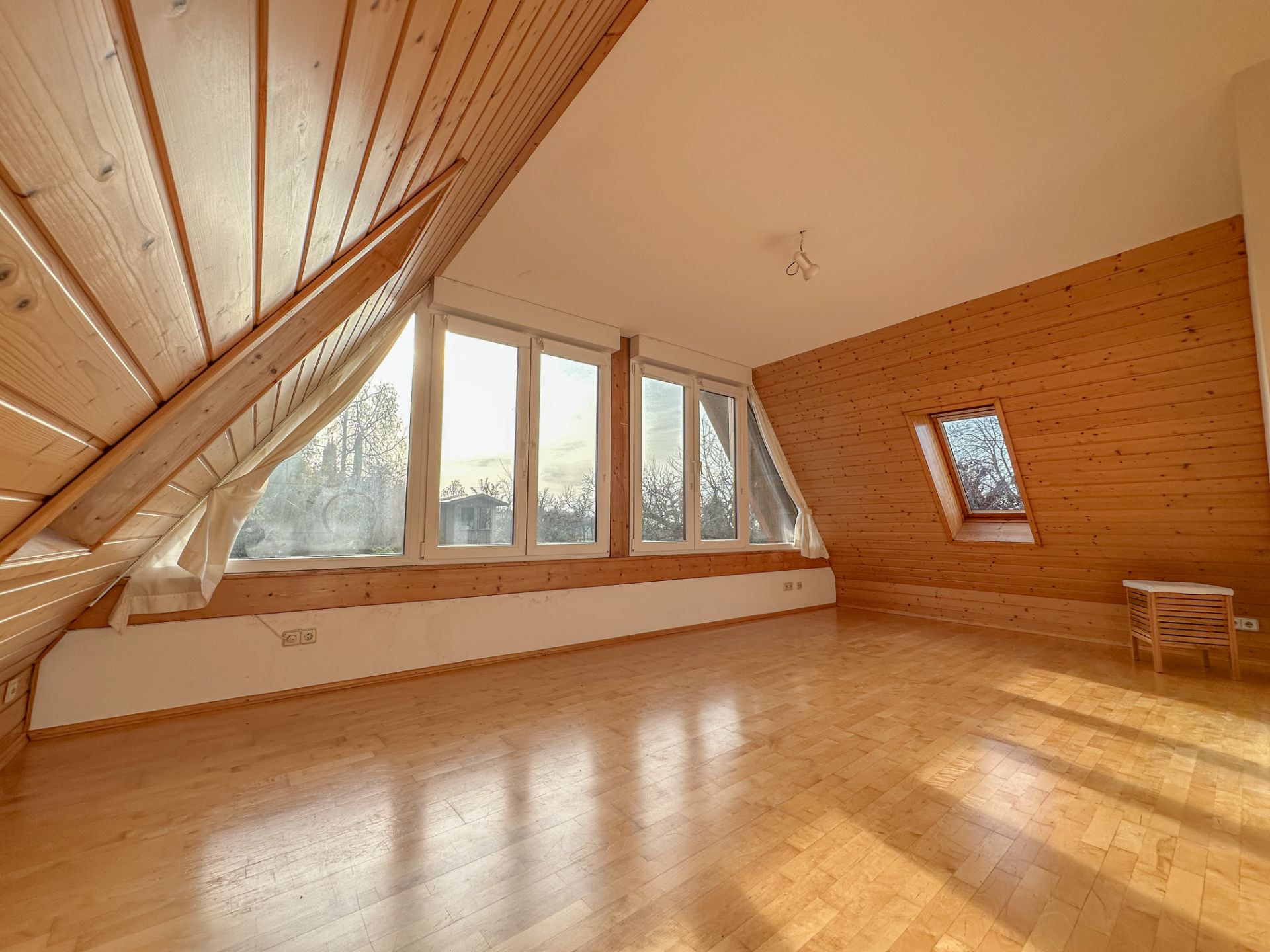 Heller Dachraum mit großen Fenstern, Holzverkleidung und Parkettboden.