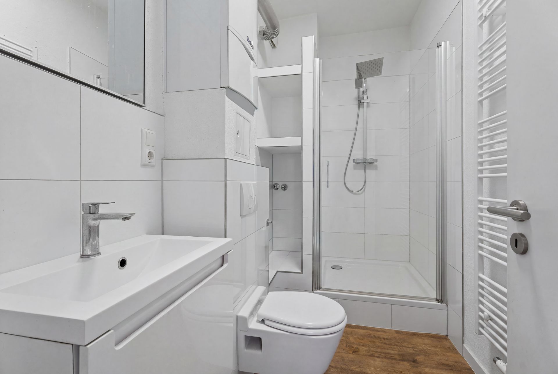 Modernes Bad mit Dusche, Waschbecken, Toilette, weißen Fliesen und Handtuchheizkörper.