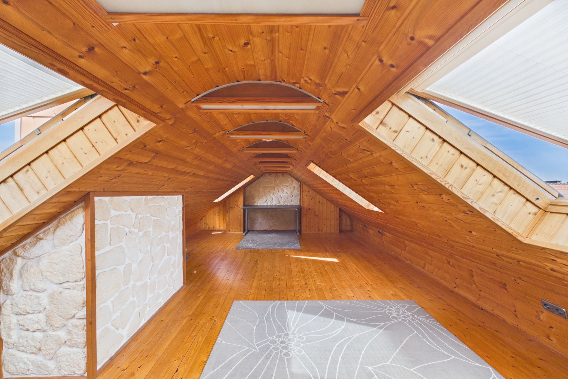 Heller Dachboden mit Holzverkleidung, Teppich und schrägen Fenstern.