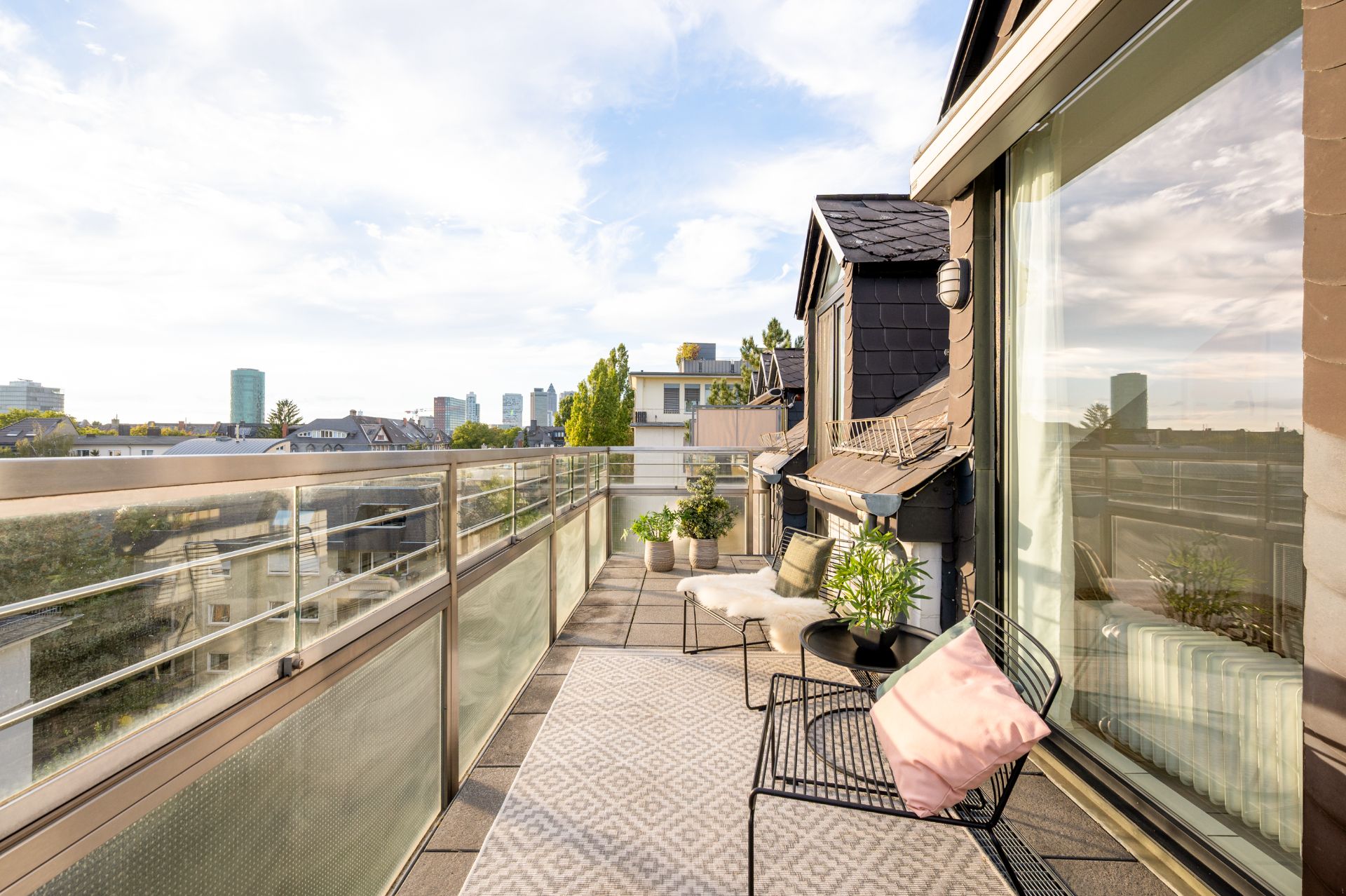 Großer Balkon mit Sitzmöbeln, Pflanzen und Blick auf die Stadt.