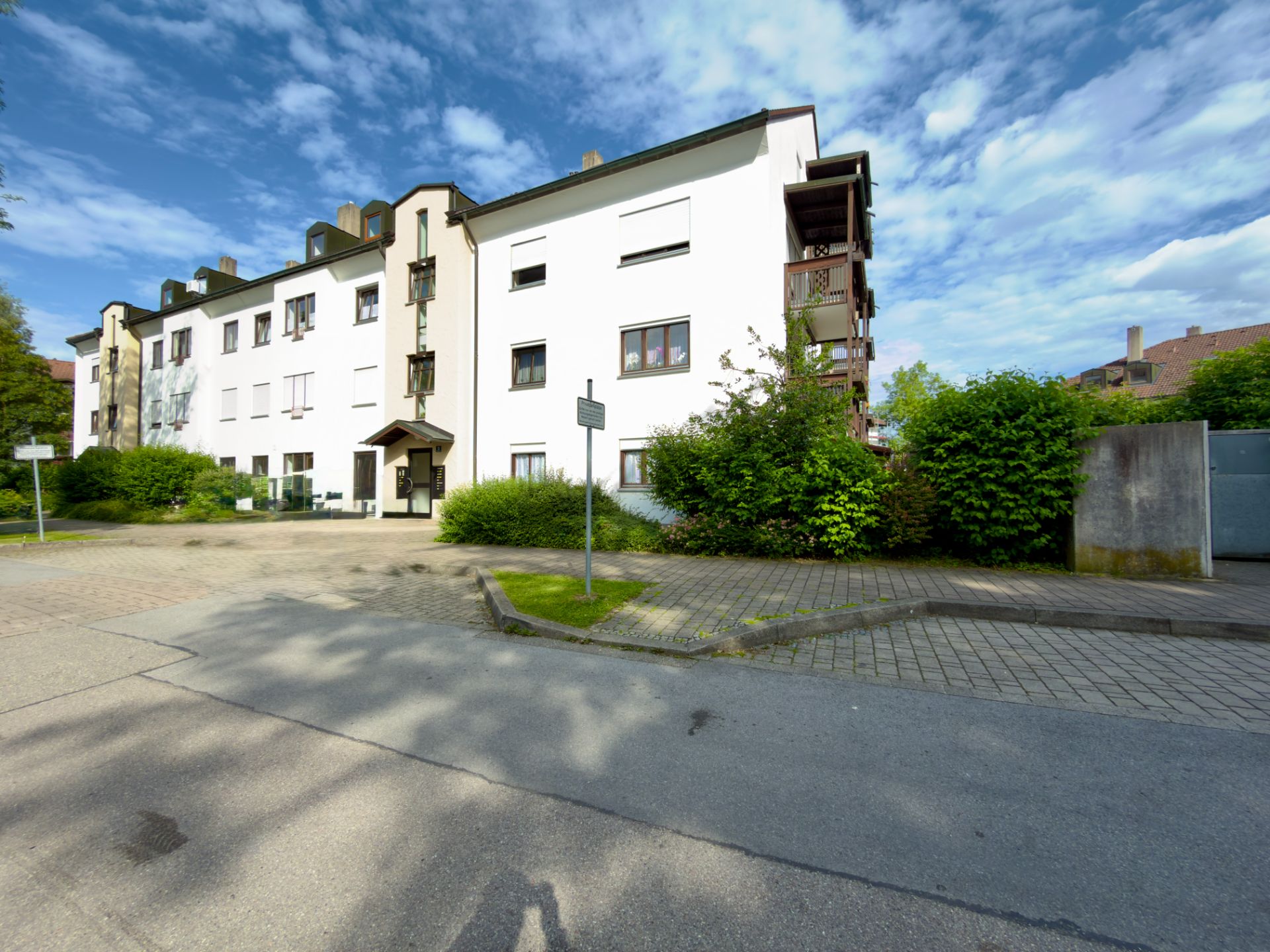 Mehrfamilienhaus mit weißer Fassade, mehreren Stockwerken und Balkonen, umgeben von Grünanlagen.
