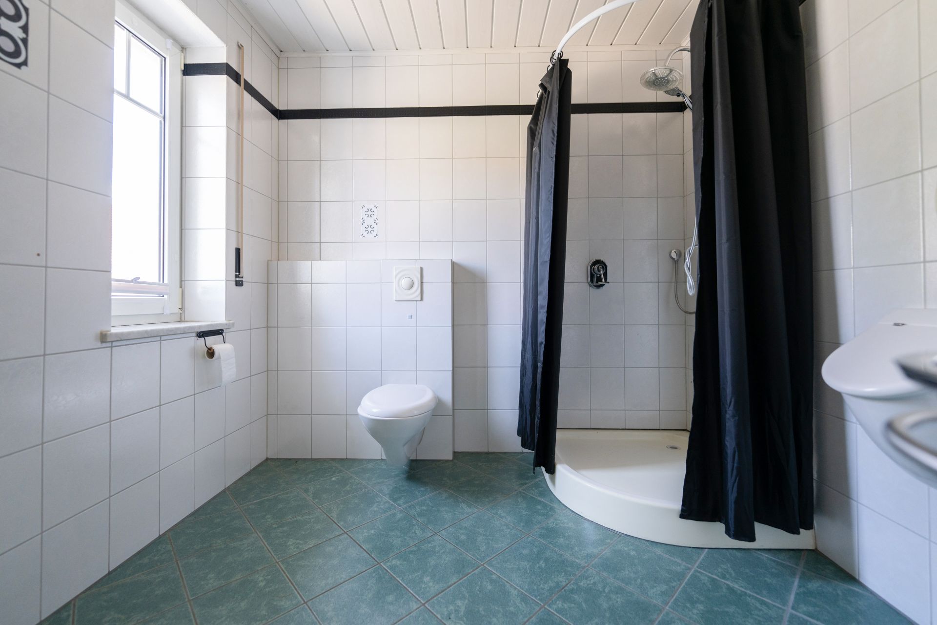 Helles Badezimmer mit WC, Dusche mit schwarzem Vorhang und Fenster.