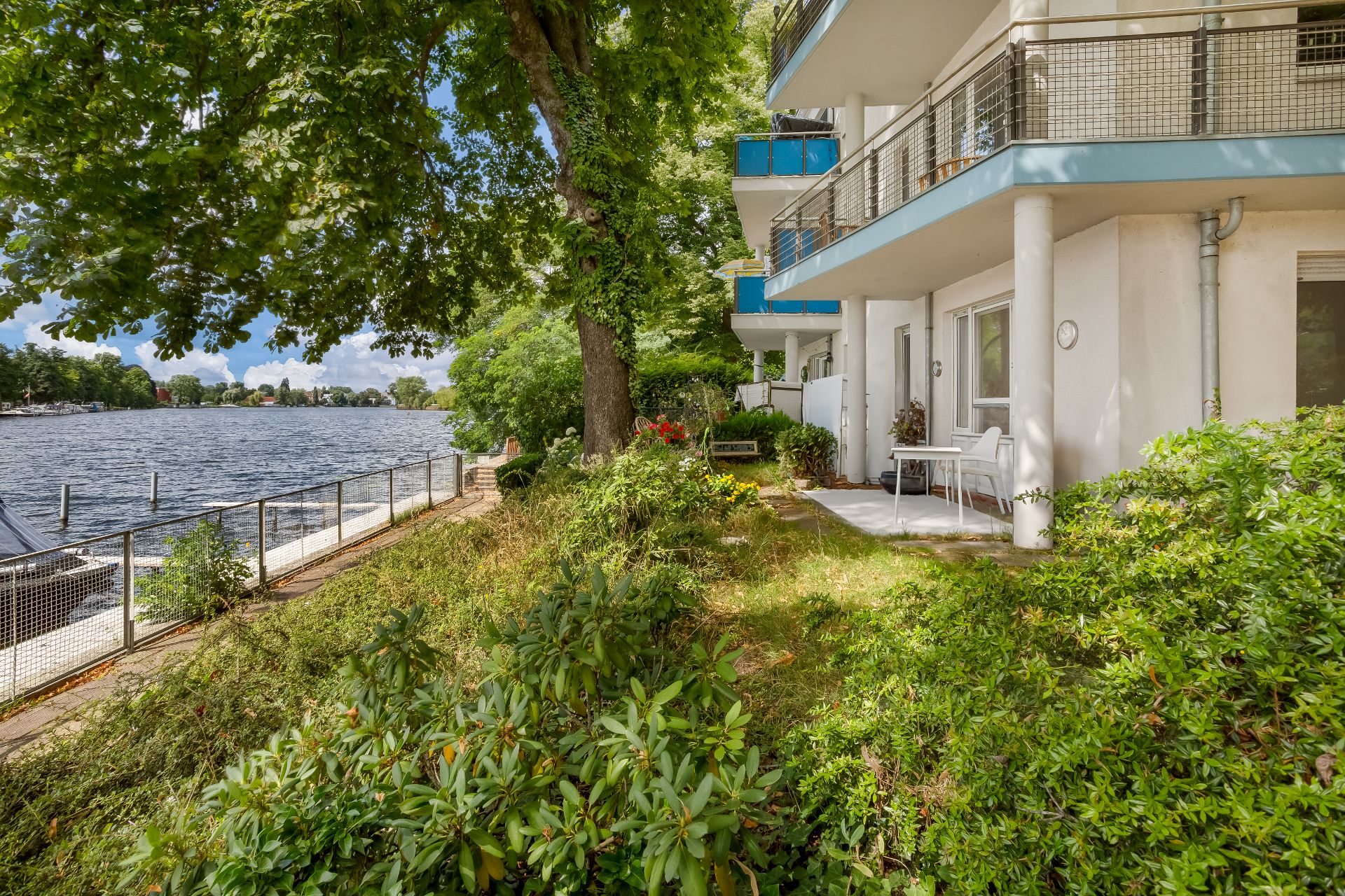 Wohnhaus mit Terrasse am Fluss, umgeben von Bäumen und viel Grün.