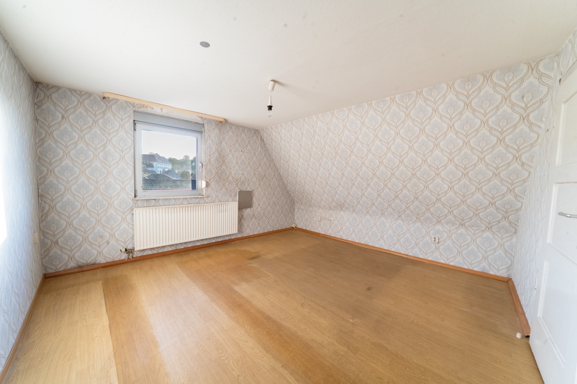 Leeres Zimmer mit Tapeten, Holzfußboden, Fenster und Heizung.