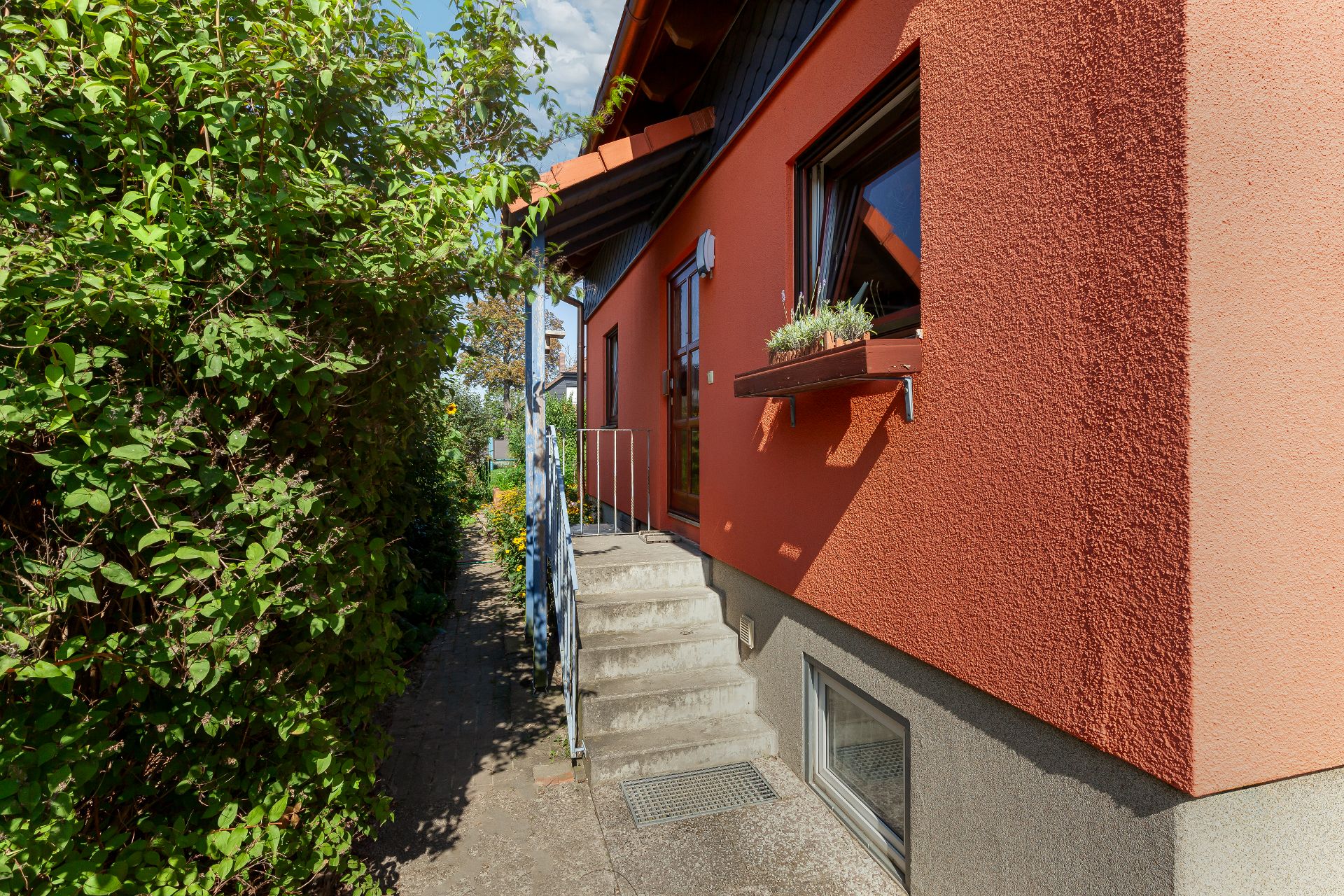 Eingangsbereich eines roten Wohnhauses mit Treppe und bepflanztem Fensterbrett.