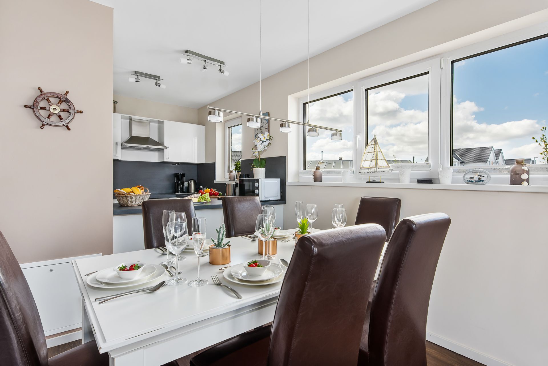 Essbereich mit gedecktem Tisch und Blick in eine moderne Küche mit großen Fenstern.